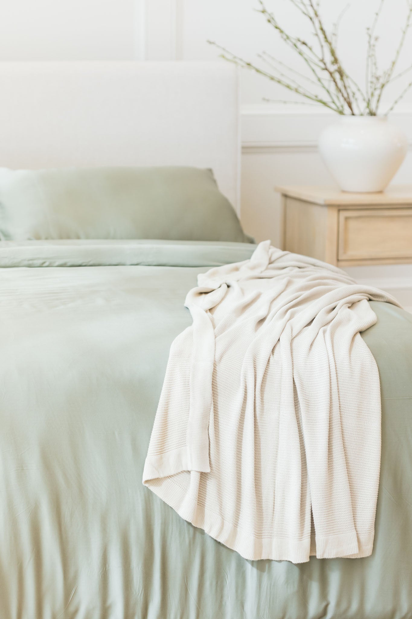 Driftwood cloud knit blanket draped over bed with sage sheets 