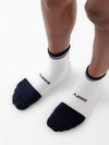 A close-up image of a person's feet wearing a pair of Cozy Earth's Essential Quarter Socks from the 2-Pack collection, featuring white socks with black toes, heels, and cuffs. The left sock is emblazoned with "EARTH," while the right one displays "COZY." The person is standing on a light background. |Color:Eclipse