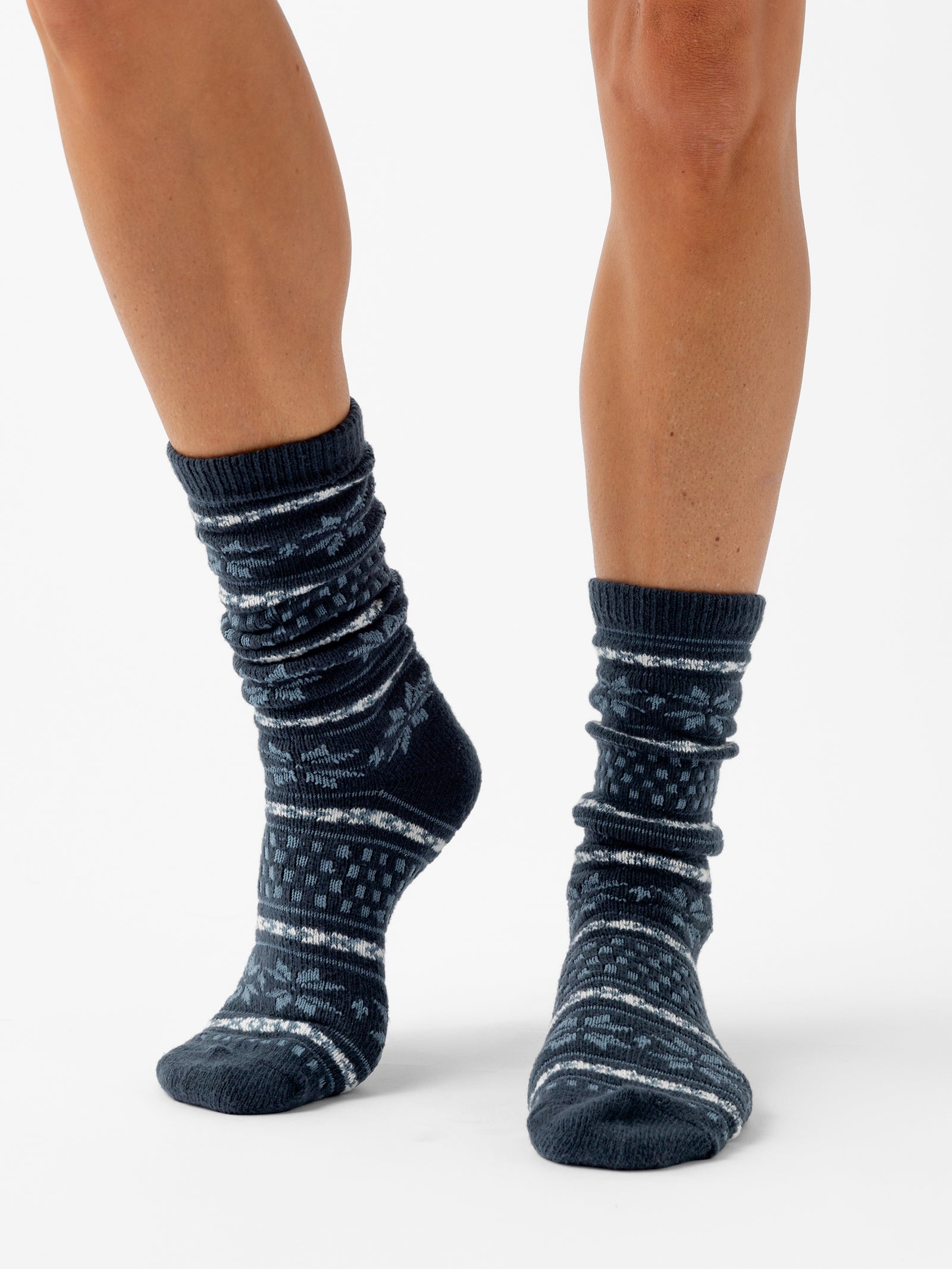 A person stands with a white background wearing Snowflake Plush Lounge Socks in Eclipse 