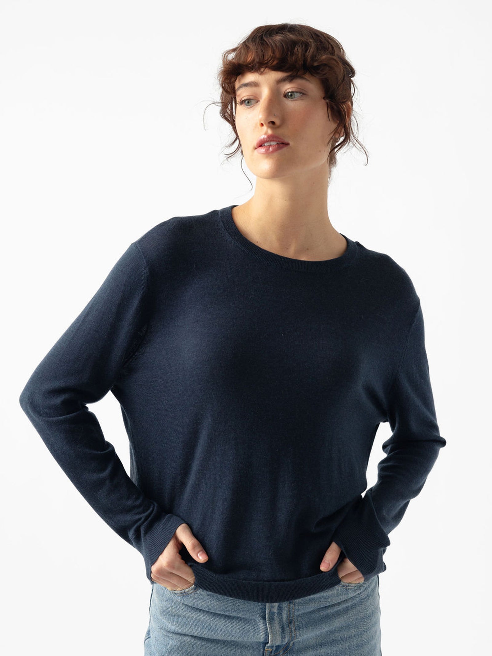 Woman with serious look wearing jeans and an eclipse airknit sweater with white background 