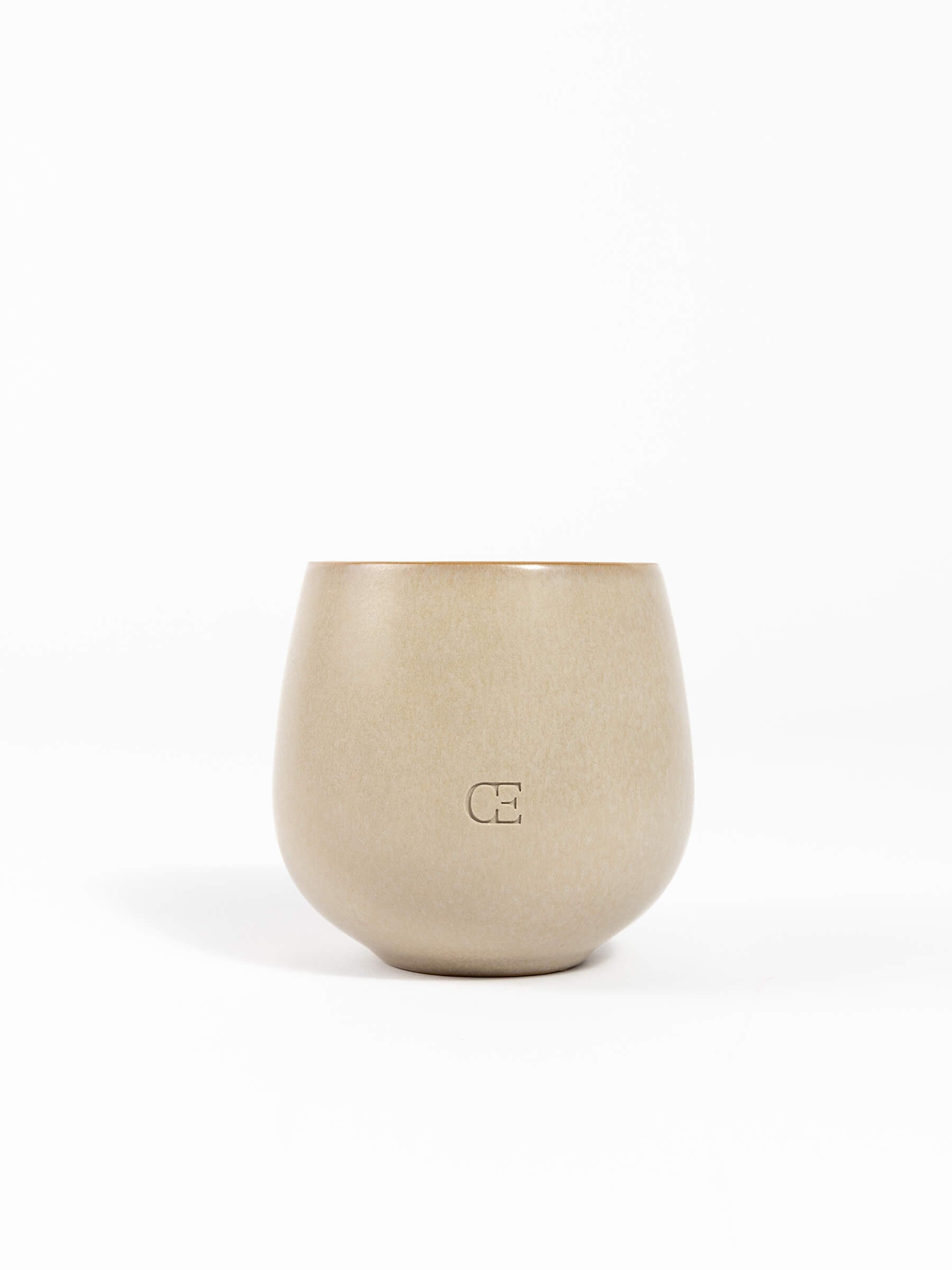 A beige, round ceramic Candle EMBER by Cozy Earth with a matte finish and "CE" embossed on the front, shown against a plain white background.