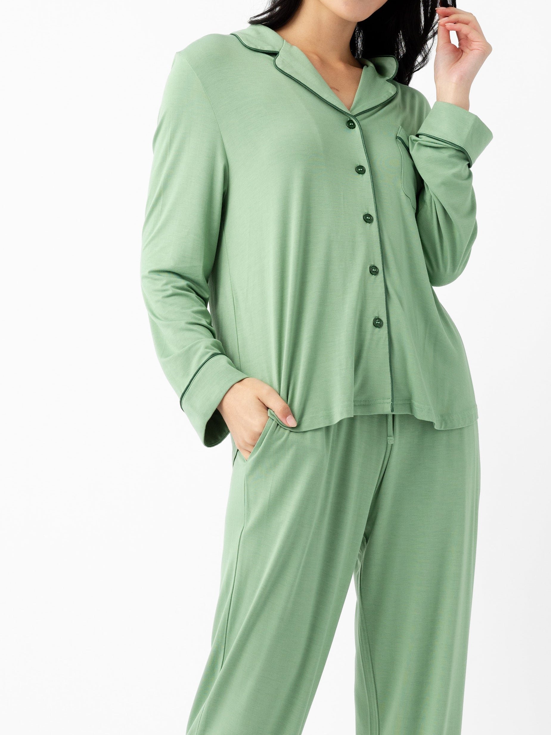A woman wears the Cozy Earth Last Chance Women's Bamboo Stretch-Knit Long Sleeve Pajama Set in light green, featuring a loose fit, button-up top, and matching pants, with one hand in her pocket against a plain white background.