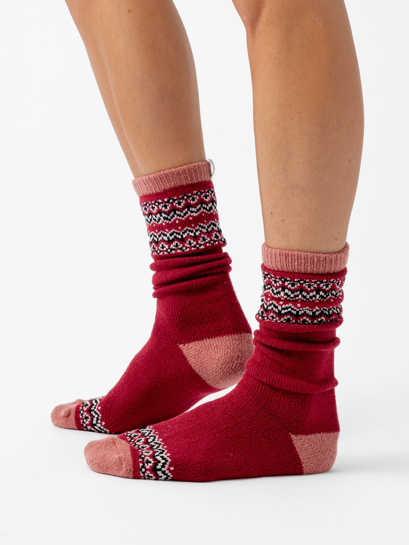 A person stands facing sideways in front of a white background wearing Fair Isle Plush Lounge Socks in Garnet. 