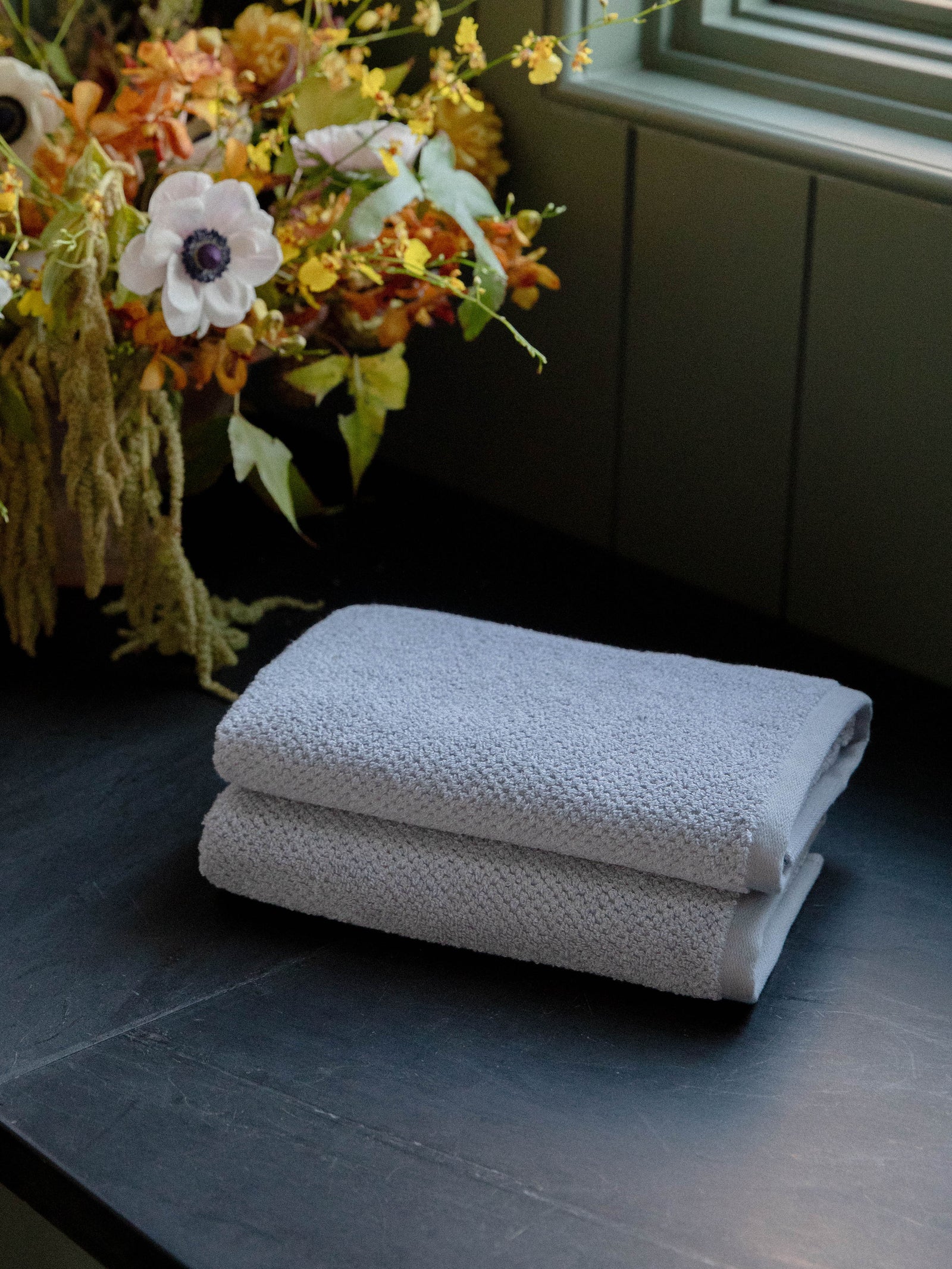 Nantucket Hand Towels in the color Heathered Harbor Mist. Photo of Nantucket Hand Towels taken with the bath towels resting on a countertop in a bathroom. 