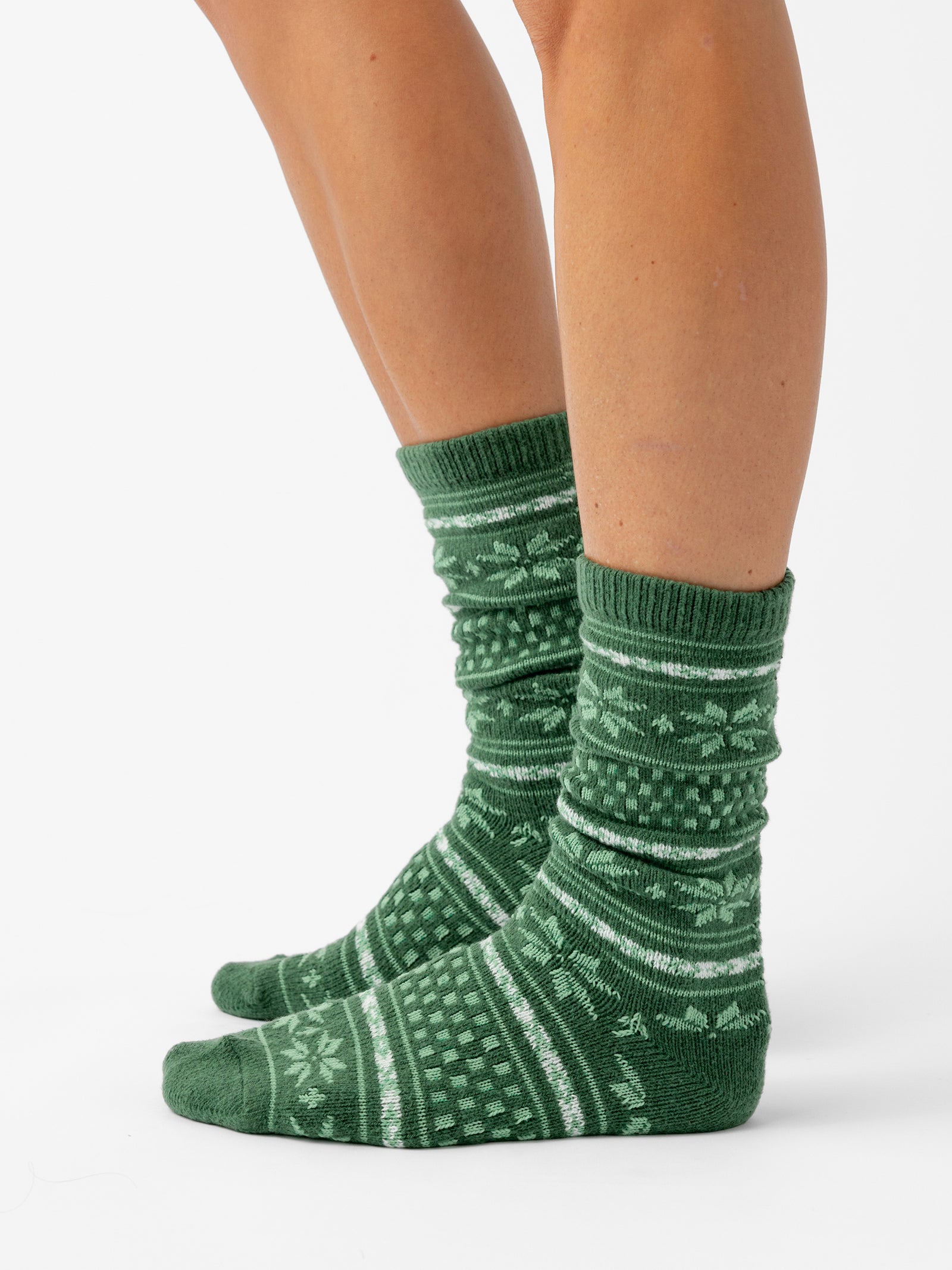 A person stands sideways with a white background wearing Snowflake Plush Lounge Sock in Jade 