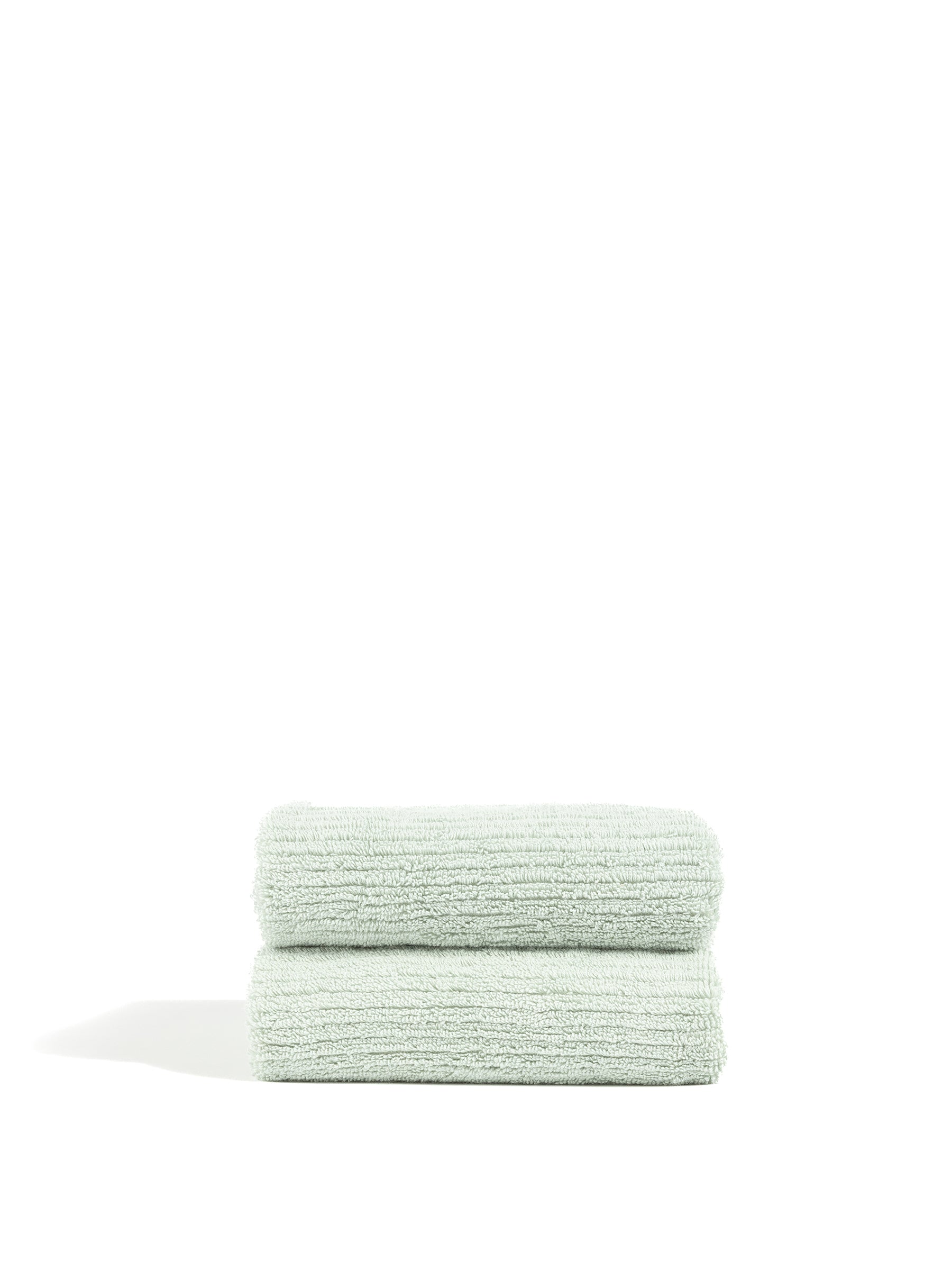 Two neatly folded Ribbed Terry Hand Towels from Cozy Earth, in a light green hue, are stacked on top of each other against a plain white background. The towels feature a soft, plush texture and boast a clean, minimalist appearance. |Color:Laurel