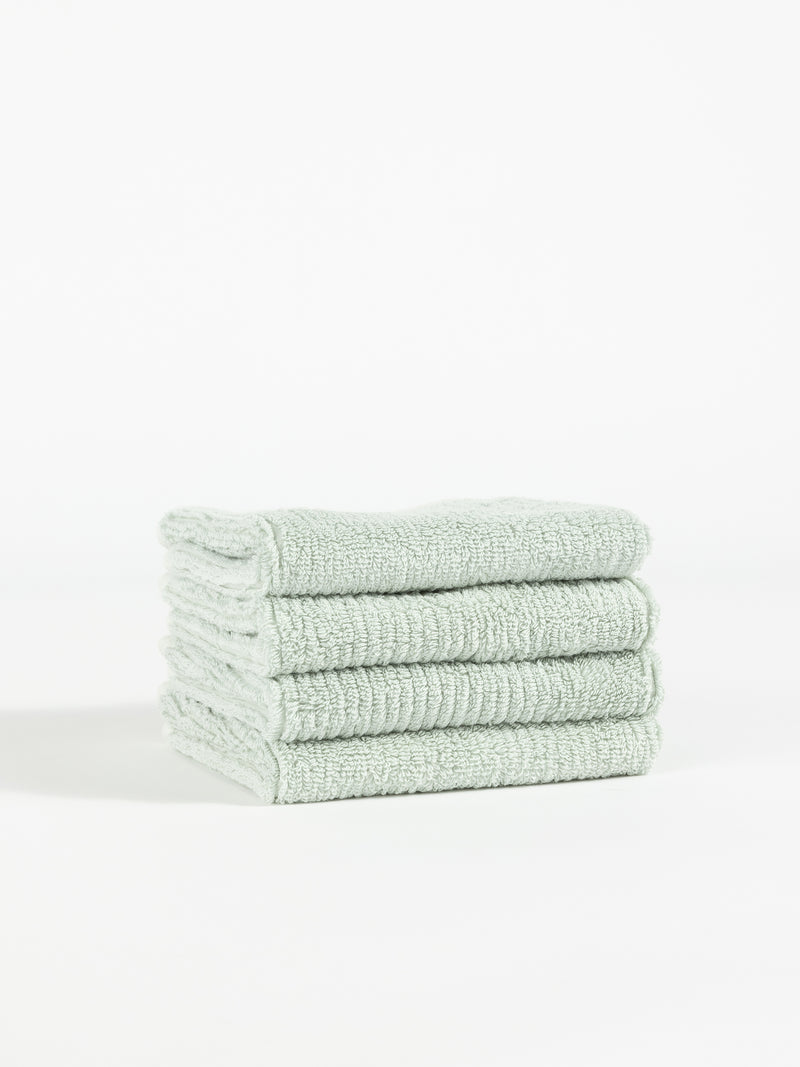 A neatly stacked pile of four light gray Ribbed Terry Washcloths from Cozy Earth is shown against a plain white background. The washcloths have a soft, fluffy texture, suggesting a comfortable and absorbent fabric.