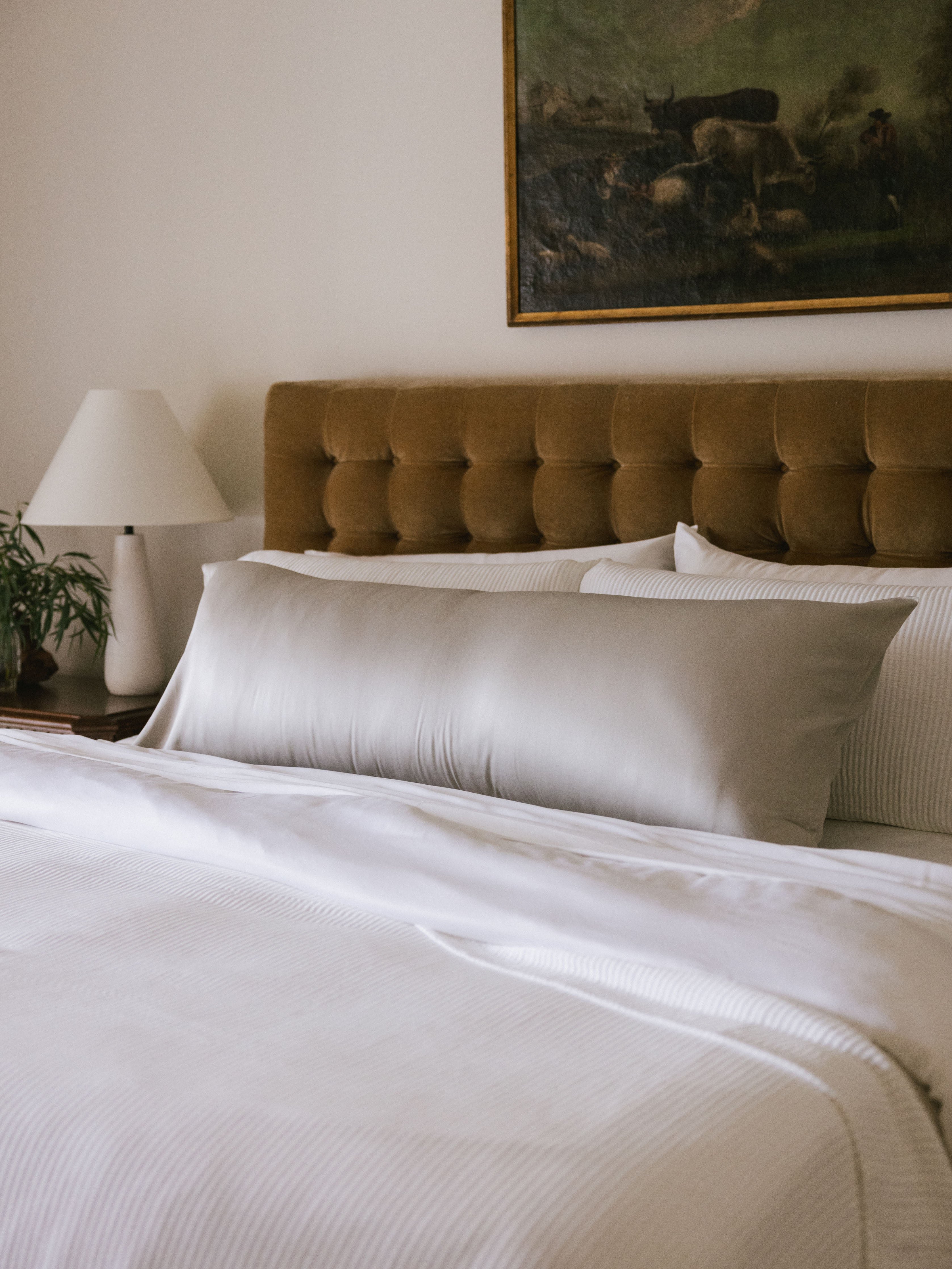 Body pillow with light grey case on bed 