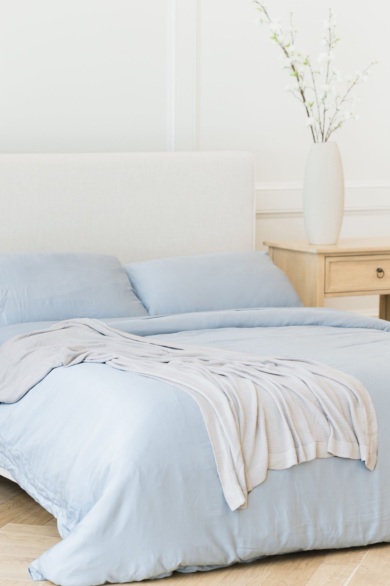 Light Grey cloud knit blanket draped over bed with harbor mist bedding 