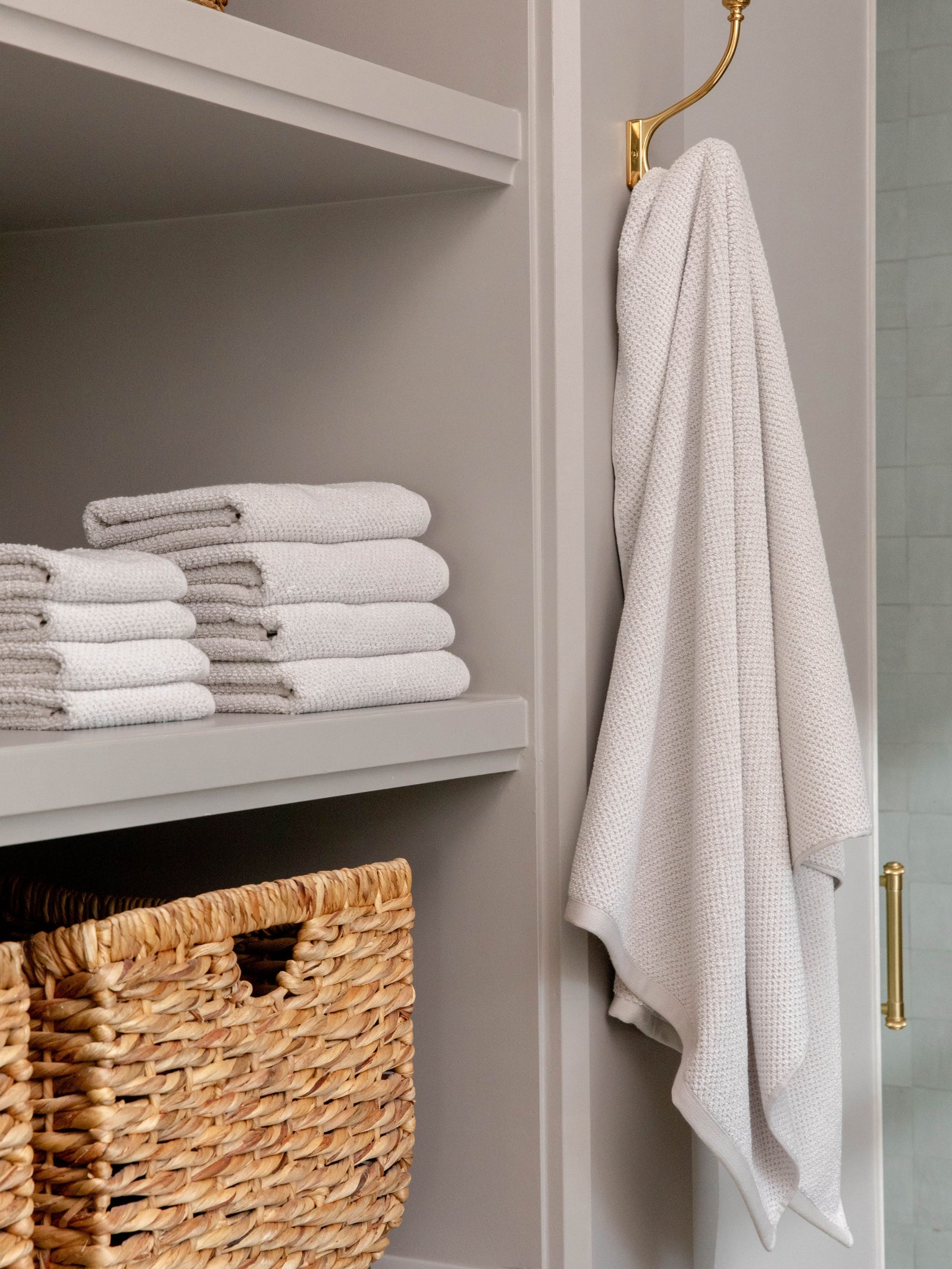 Nantucket Bath Sheets in the color Heathered Light Grey. Photo of Nantucket Bath Sheets taken as Nantucket hand towels, wash clothes, and bath towels are neatly placed on shelves in a bathroom. 