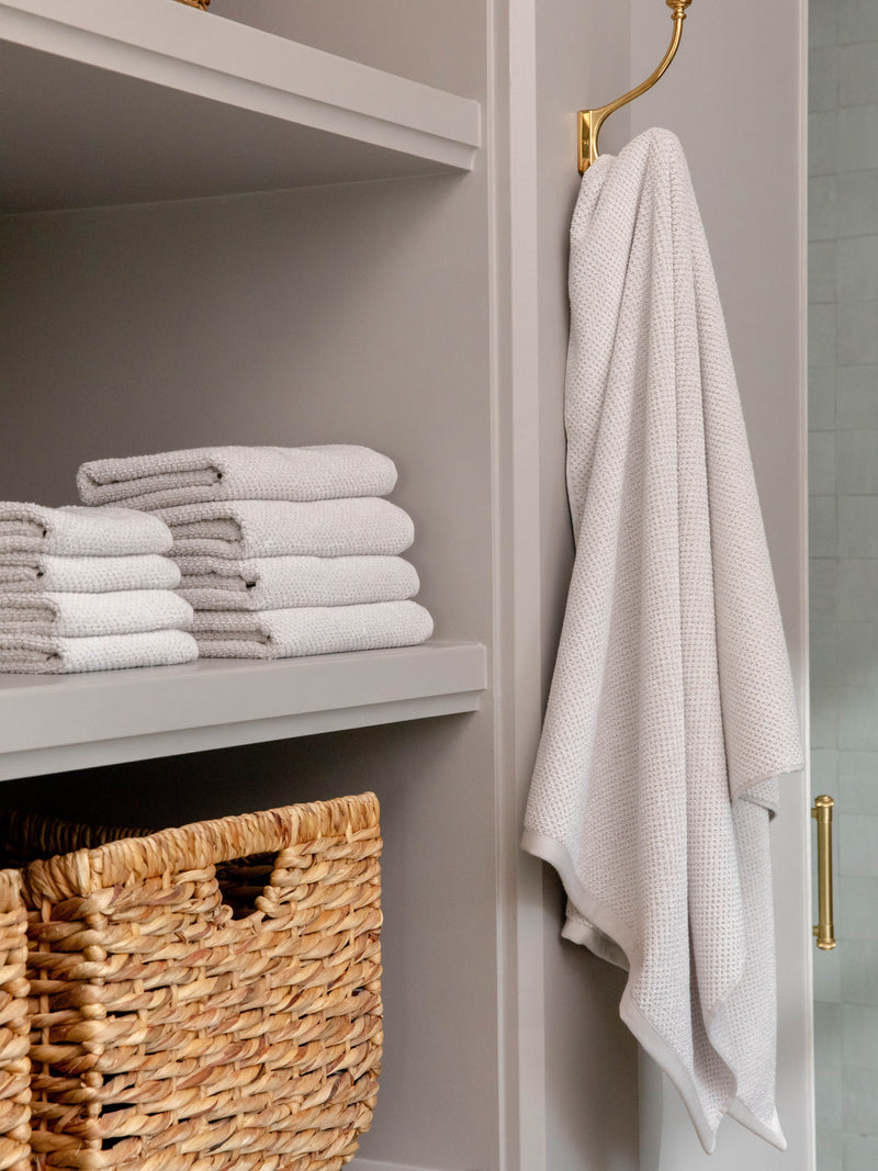 Nantucket Bath Sheets in the color Heathered Light Grey. Photo of Nantucket Bath Sheets taken as Nantucket hand towels, wash clothes, and bath towels are neatly placed on shelves in a bathroom.