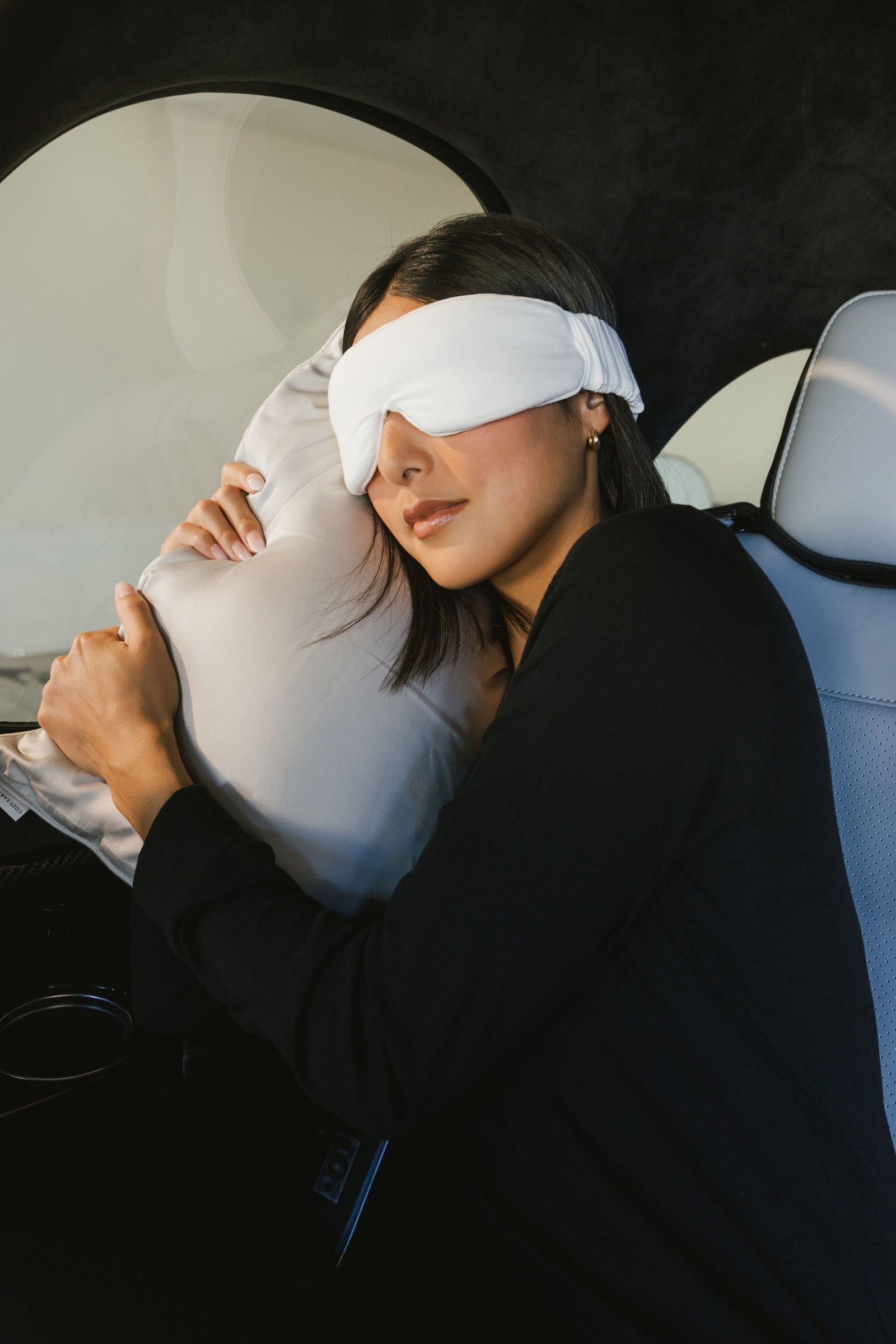 Woman with sleep mask laying in car with  travel pillow to the side 