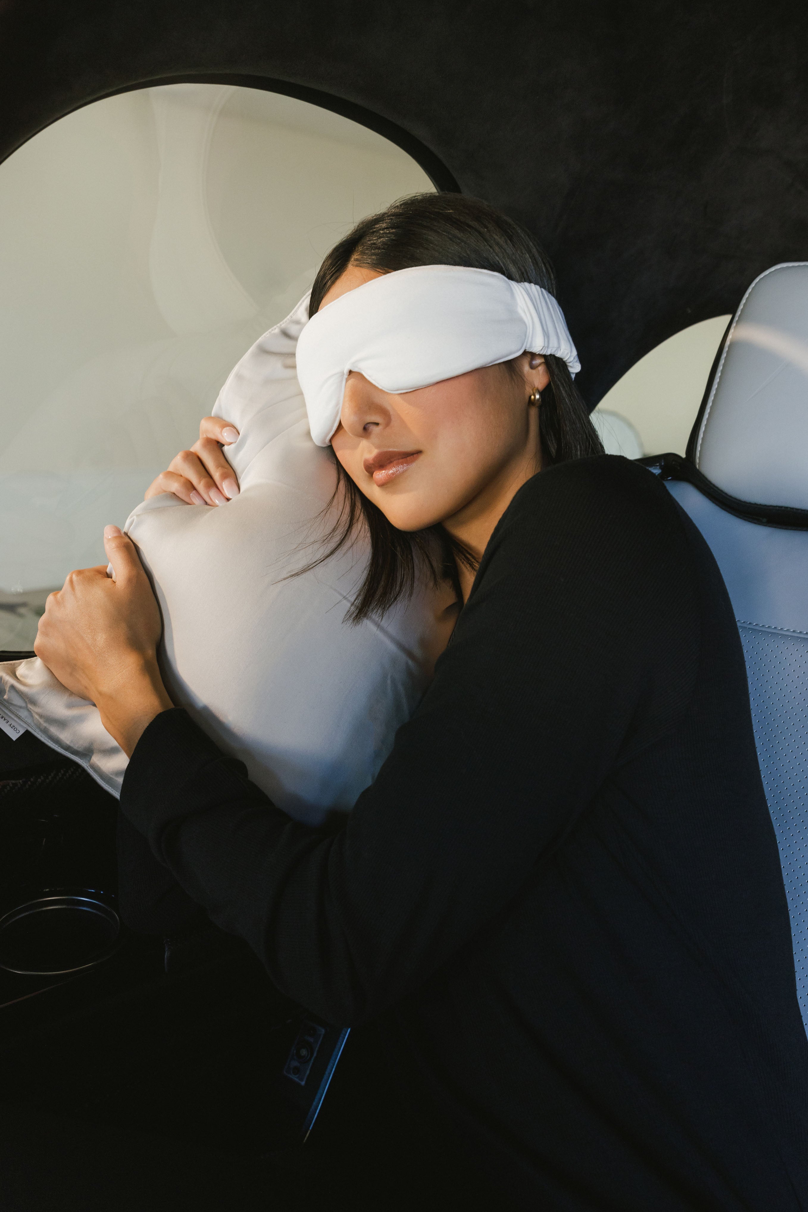 Woman with sleep mask laying in car with  travel pillow to the side |Color:Light Grey