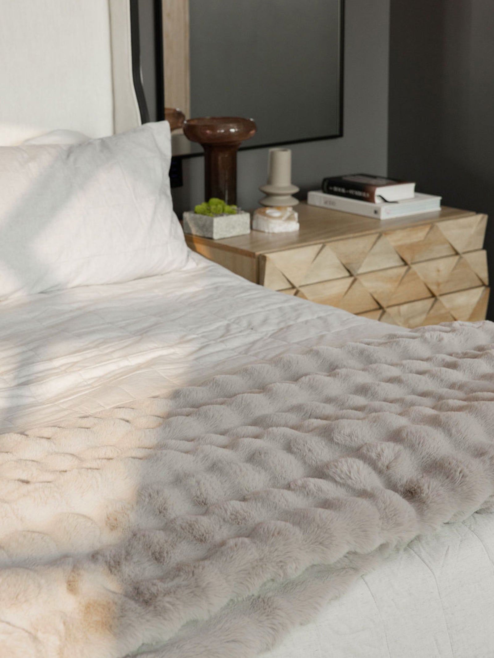 Light grey lush faux fur blanket draped over bed with white bedding 
