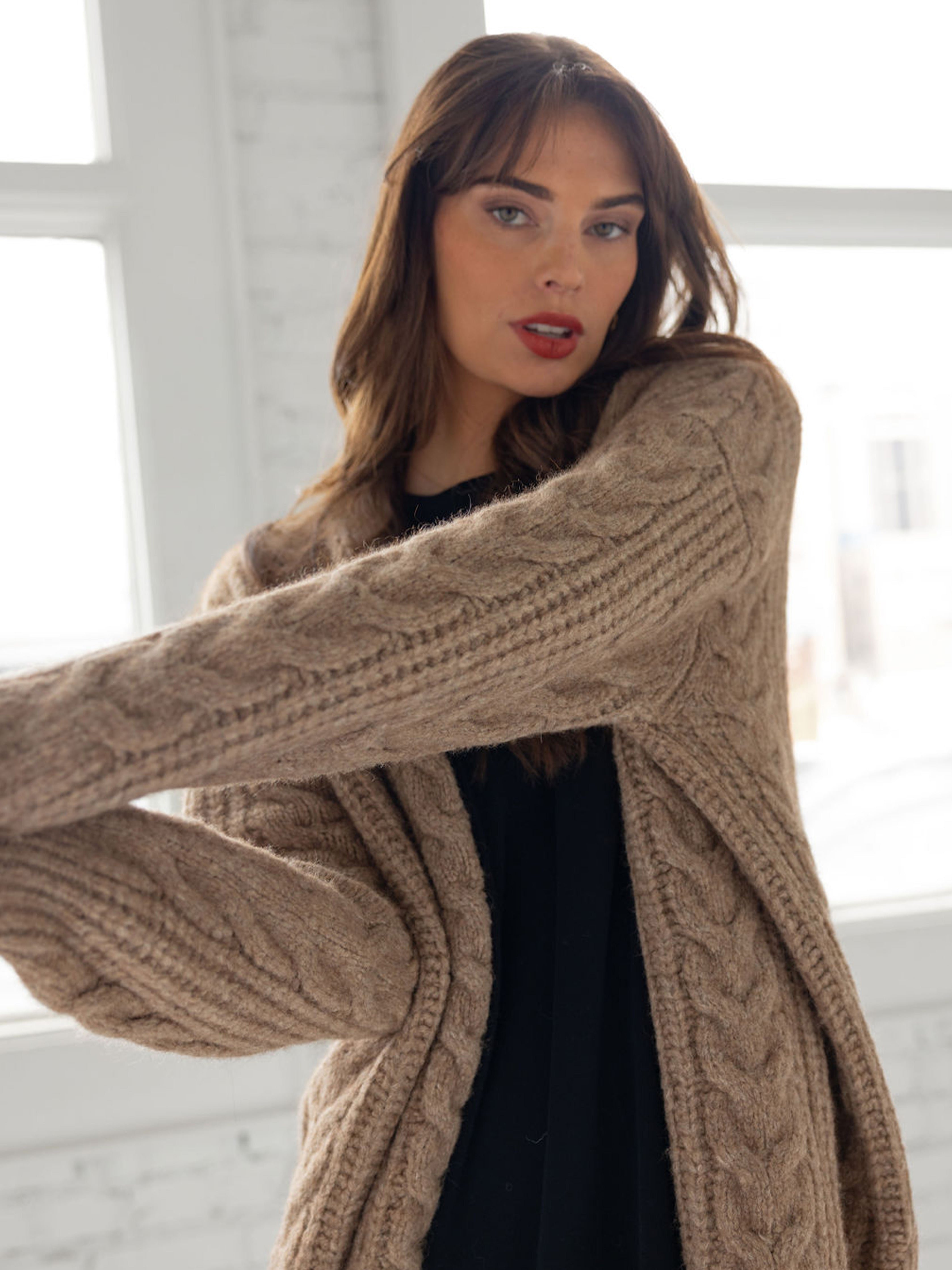 Close up of woman in mushroom cardigan over black dress in front of windows 
