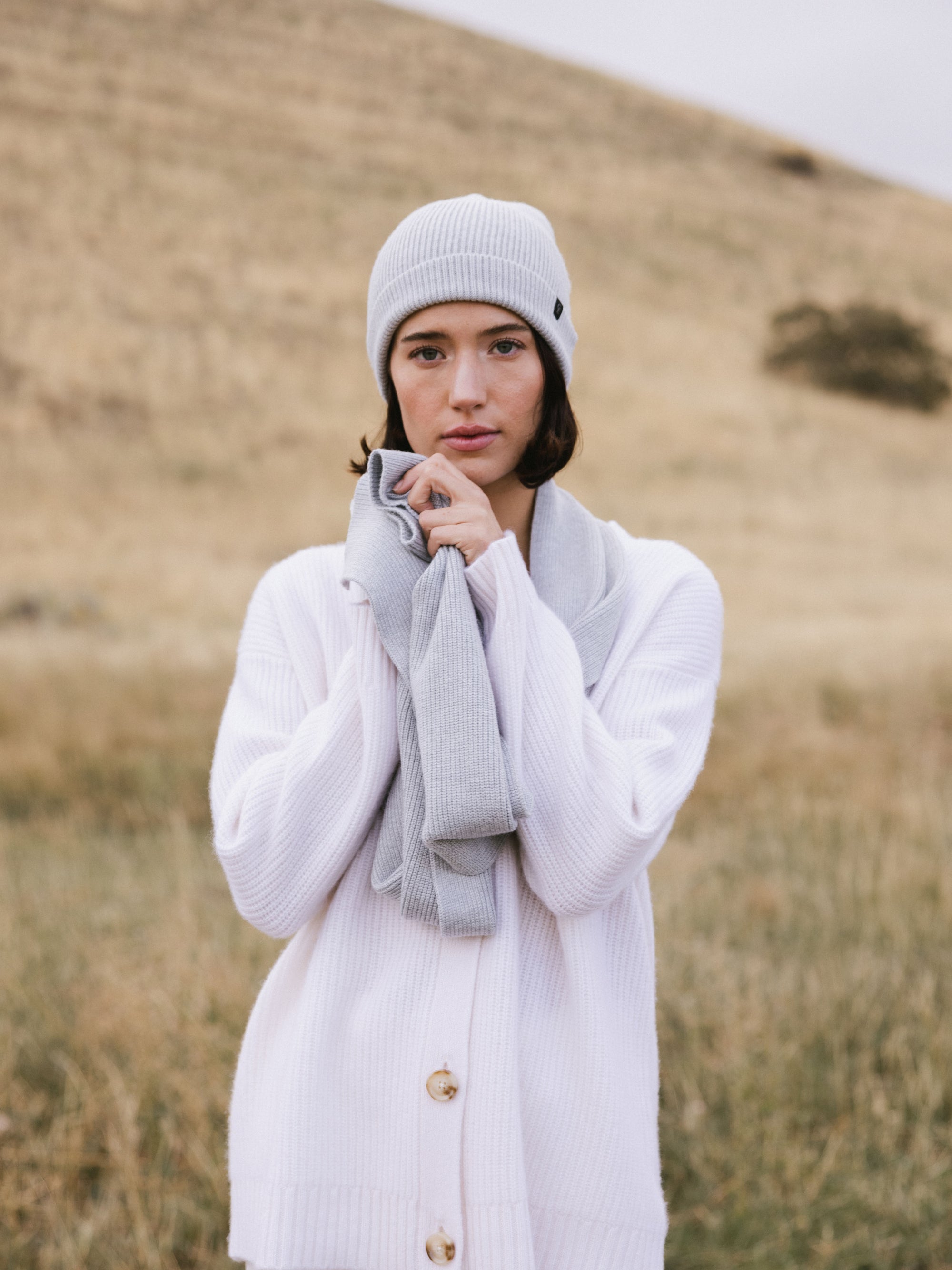 Woman wearing a light gray knit beanie and scarf in a field 