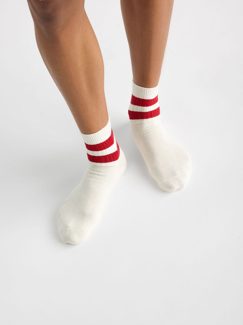 A person wearing Cozy Earth's Women's Sadie Sock in white with red stripes, shown against a neutral backdrop, highlighting their lower legs and feet. 