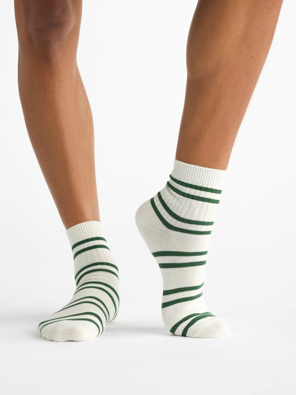 Legs in Women's Sadie Socks by Cozy Earth, featuring a plain white design with dark green horizontal stripes. One foot is flat, while the other is slightly tiptoed. 