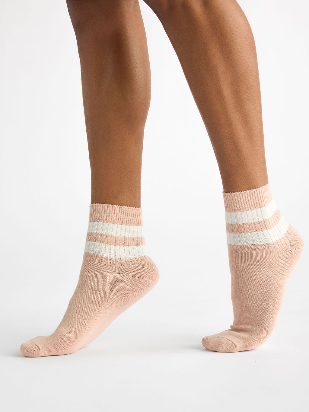 A person is wearing Cozy Earth's Women's Sadie Sock in light pink, featuring two white stripes near the top. These ankle-length socks are shown on a plain white background. |Color:Dusty Rose/Bone