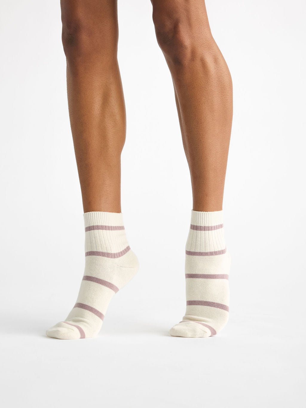 A pair of feet is wearing Cozy Earth's Women's Sadie Sock, featuring cream color with light purple horizontal stripes, against a plain white background. 