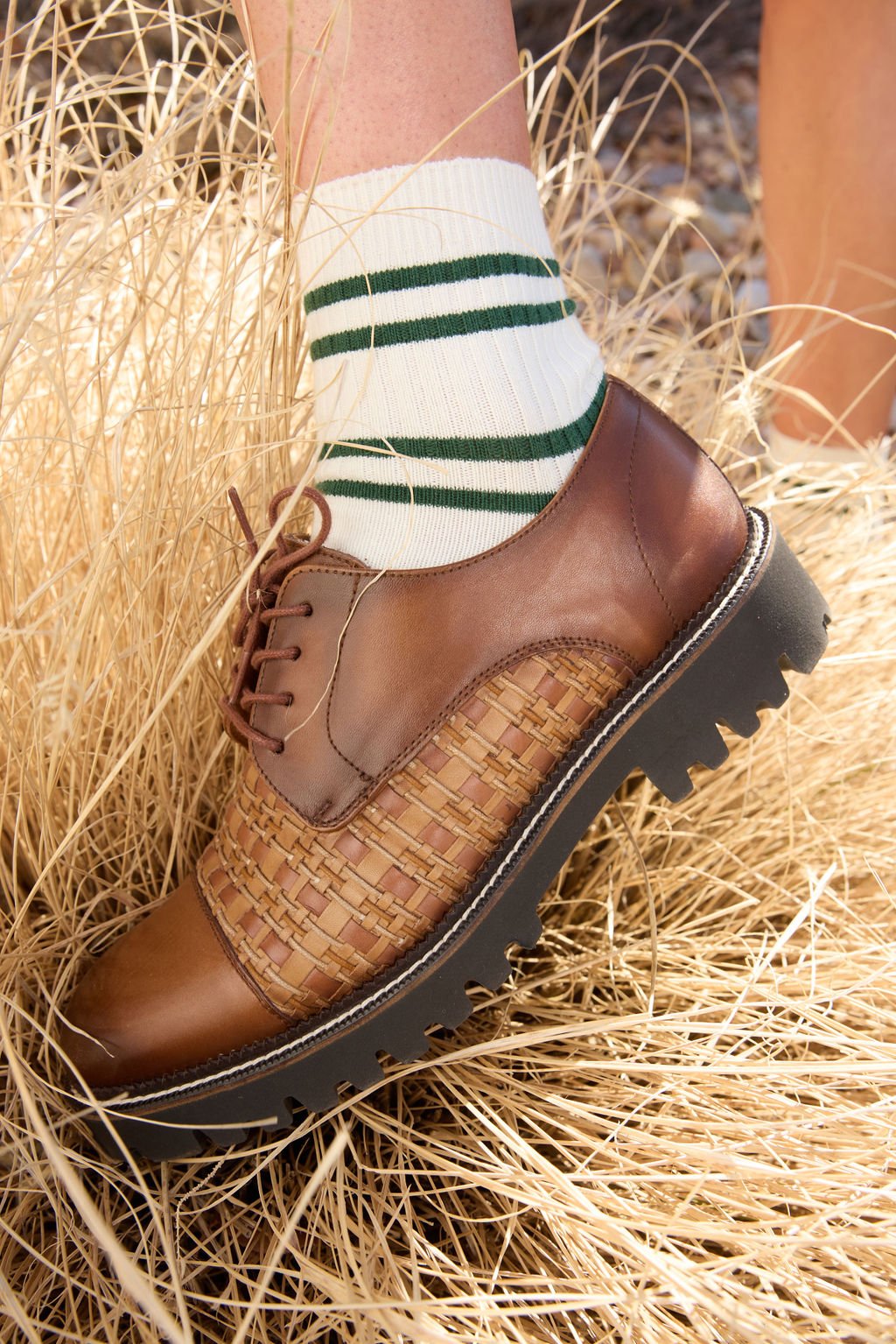 A person wearing Women's Sadie Socks by Cozy Earth, featuring green horizontal stripes wears brown shoes and stands in a yellow grass.