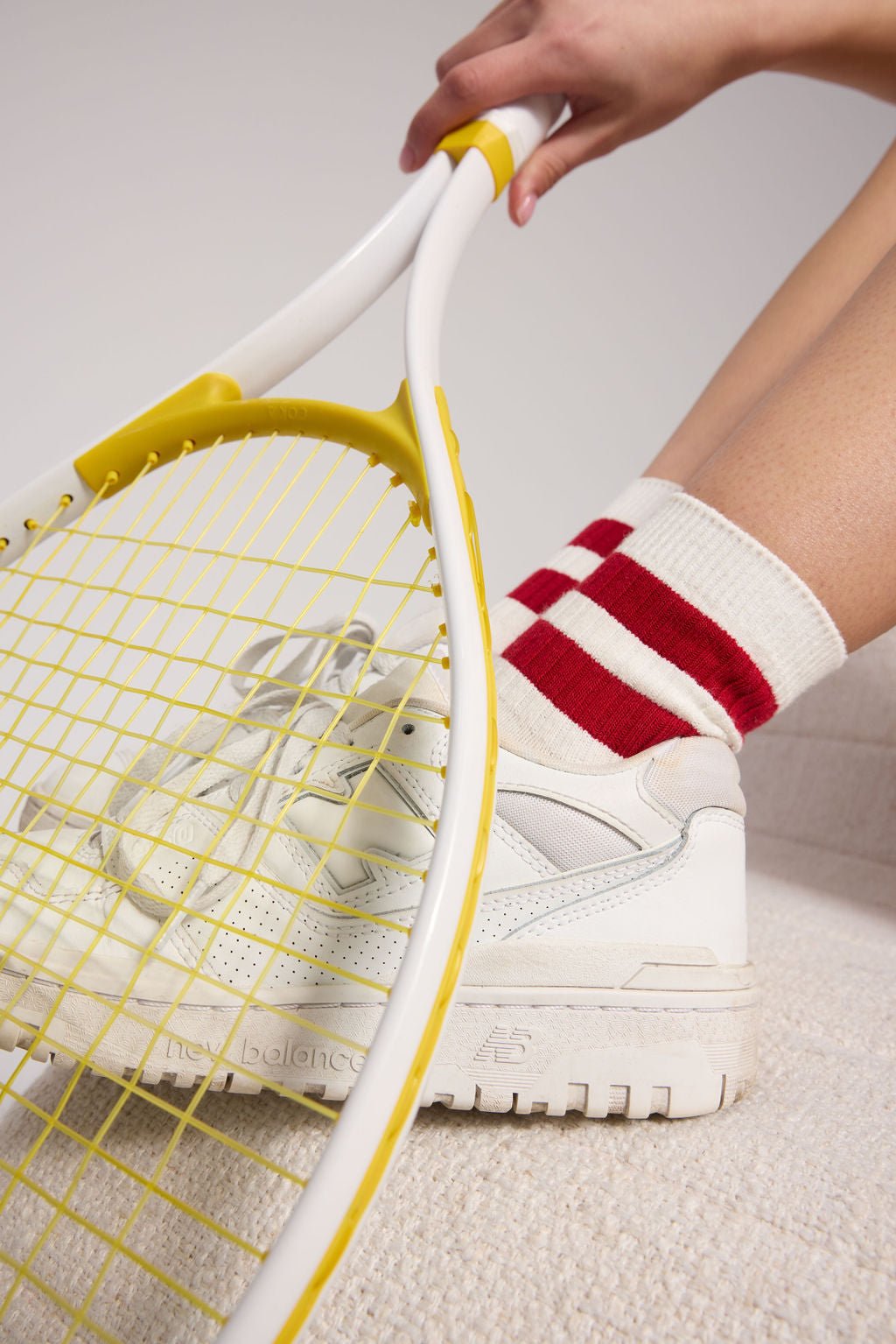 A person wearing Cozy Earth's Women's Sadie Sock, featuring a white design with two red stripes, hold a tennis racket and wears white tennis shoes. 