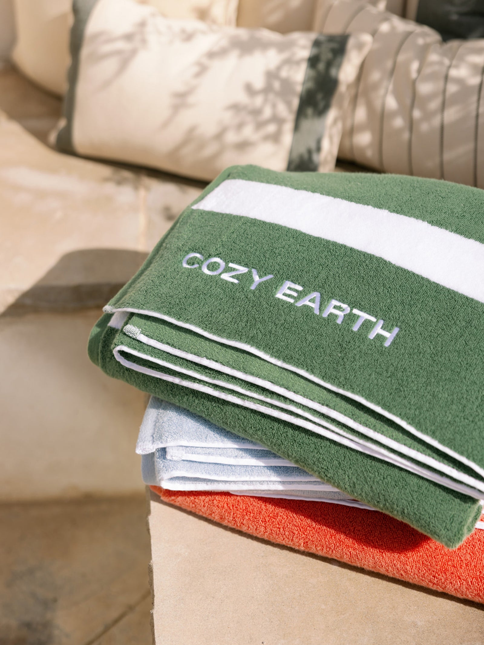 Coral, Breeze, and Sage Stripe resort towels close up neatly folded on an out door patio.