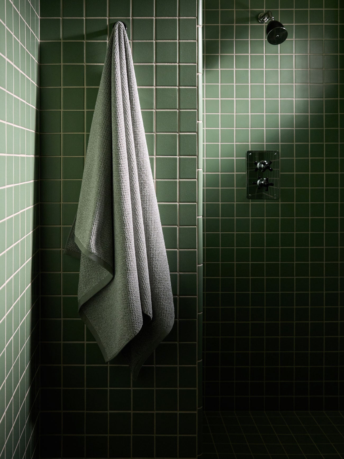 A Heathered Sage Nantucket Bath Sheet hangs in a green tiled shower. 