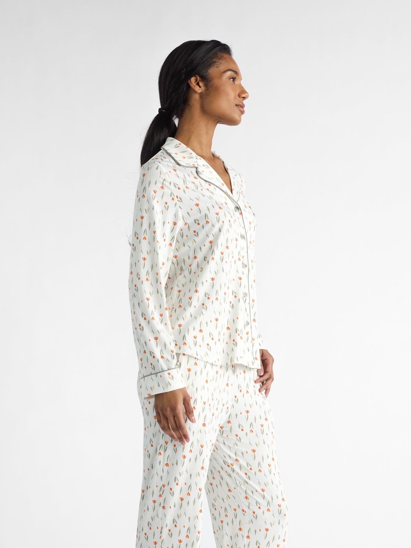 A woman with long dark hair tied back stands sideways in a Cozy Earth Women's Bamboo Stretch-Knit Long Sleeve Pajama Set featuring a colorful pattern, gazing off to the side against a plain white background. 