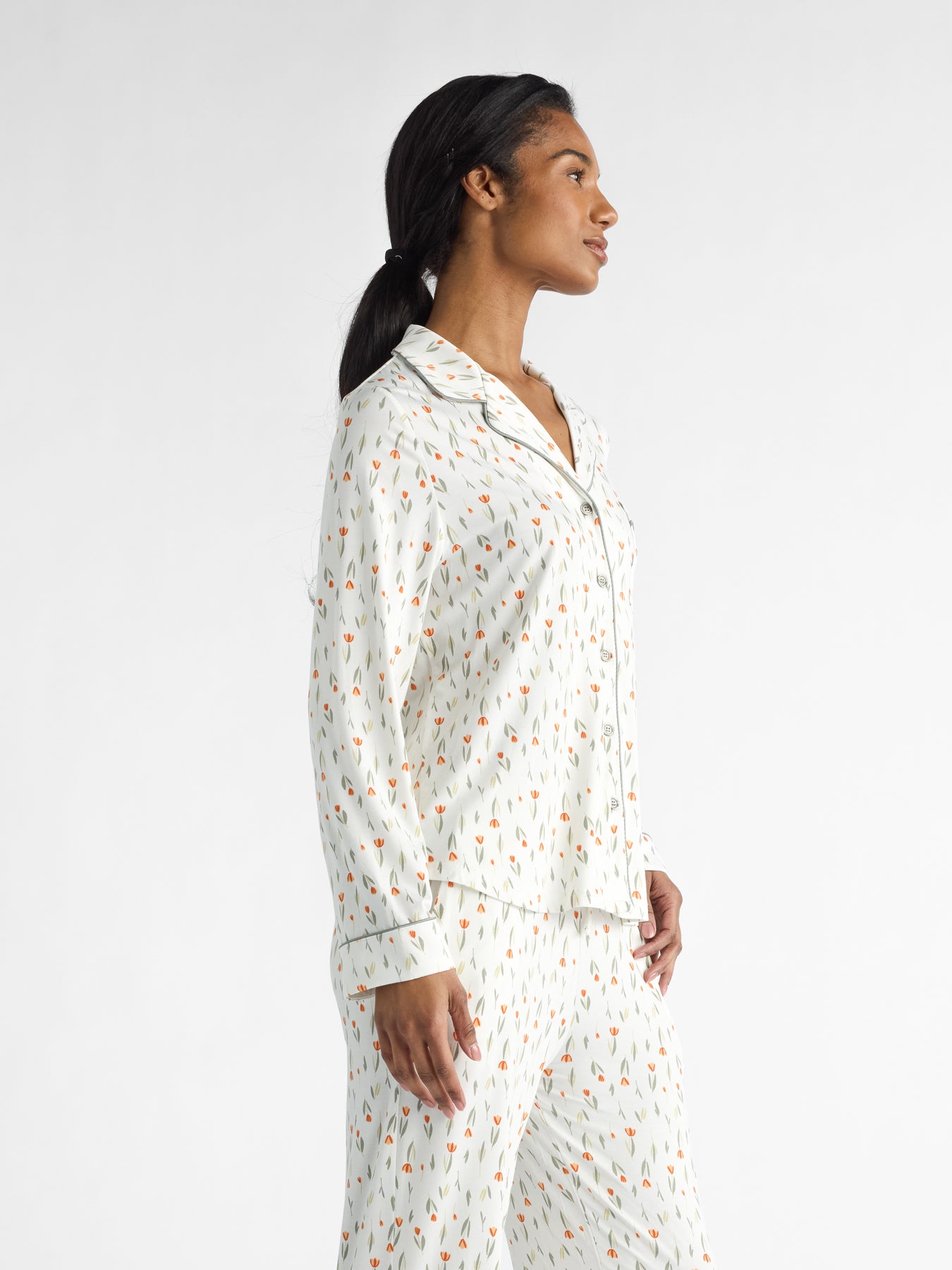 A person is shown sideways against a plain white background, wearing Cozy Earth Women's Bamboo Stretch-Knit Long Sleeve Pajama Top in white with a small, colorful design. 