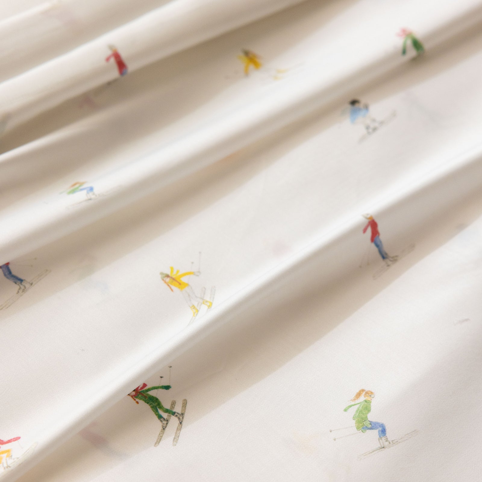 Close-up of a white Cozy Earth Bamboo Duvet Cover, adorned with small, colorful illustrations of people skiing. The duvet cover is elegantly draped in soft folds, highlighting the playful winter-themed design. 