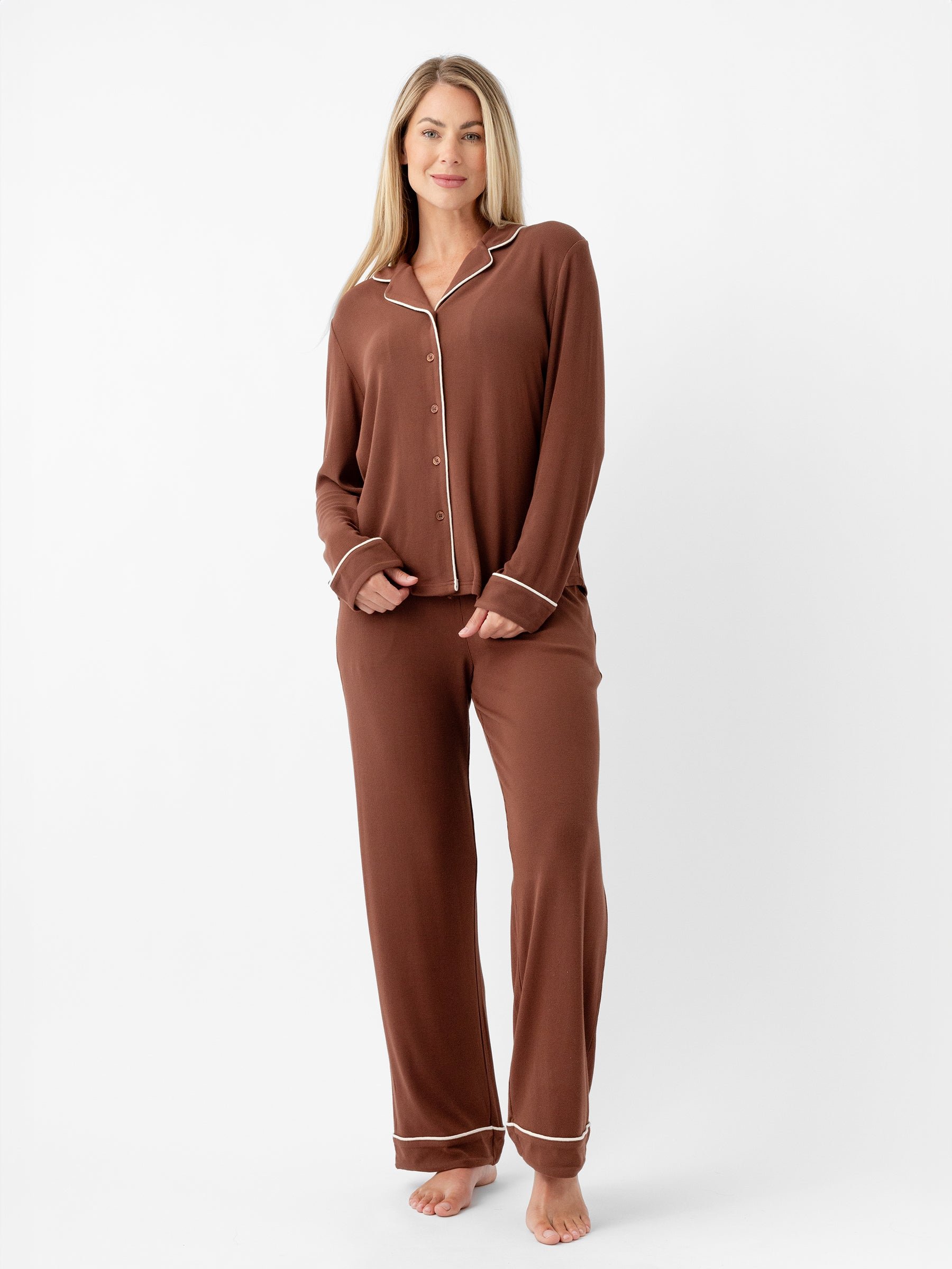 A woman stands against a plain white background, wearing the Women's Bamboo Rib Knit Classic Long Sleeve Pajama Top from Cozy Earth. She is barefoot, and her long blonde hair falls over her shoulders. She is smiling slightly and has her hands by her sides. 