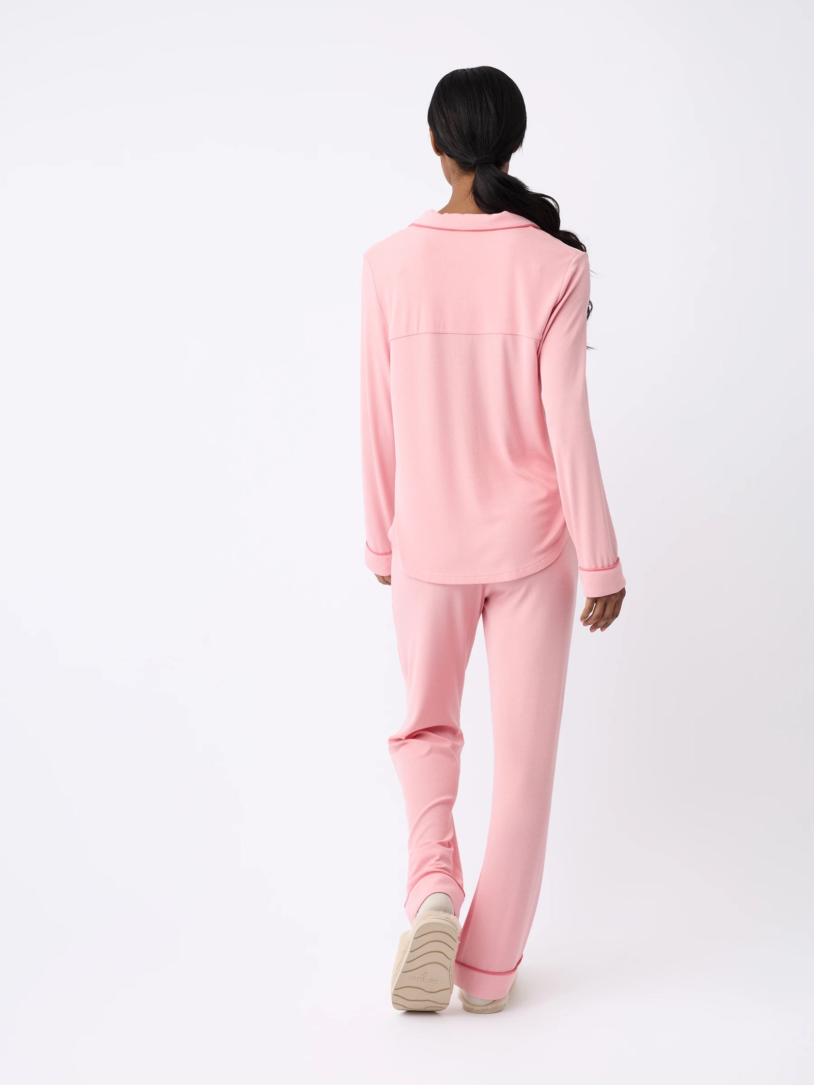 A person with long hair, seen from behind, is wearing the Cozy Earth Rib-Knit Classic Long Sleeve Pajama Set in pink. They are standing on a light background, facing away from the camera. 