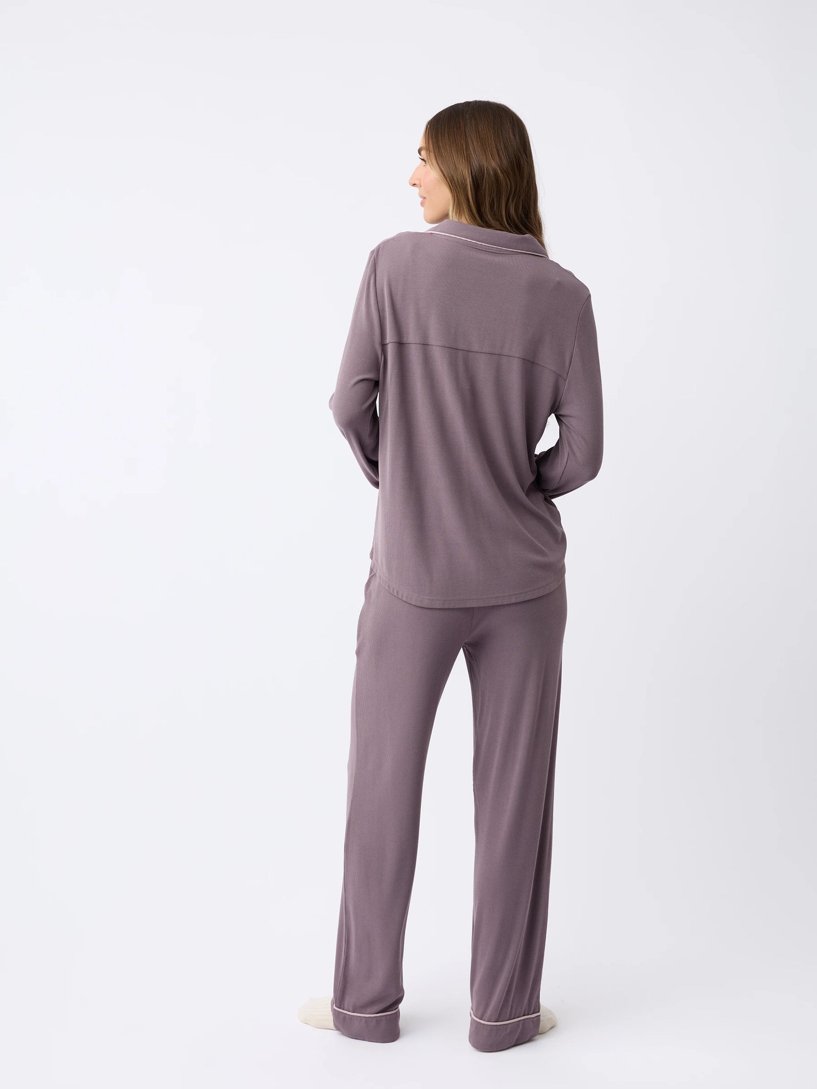 A woman with long hair, facing away on a plain white background, models the Women's Bamboo Rib-Knit Classic Pajama Pant by Cozy Earth in a soft, muted purple color. 