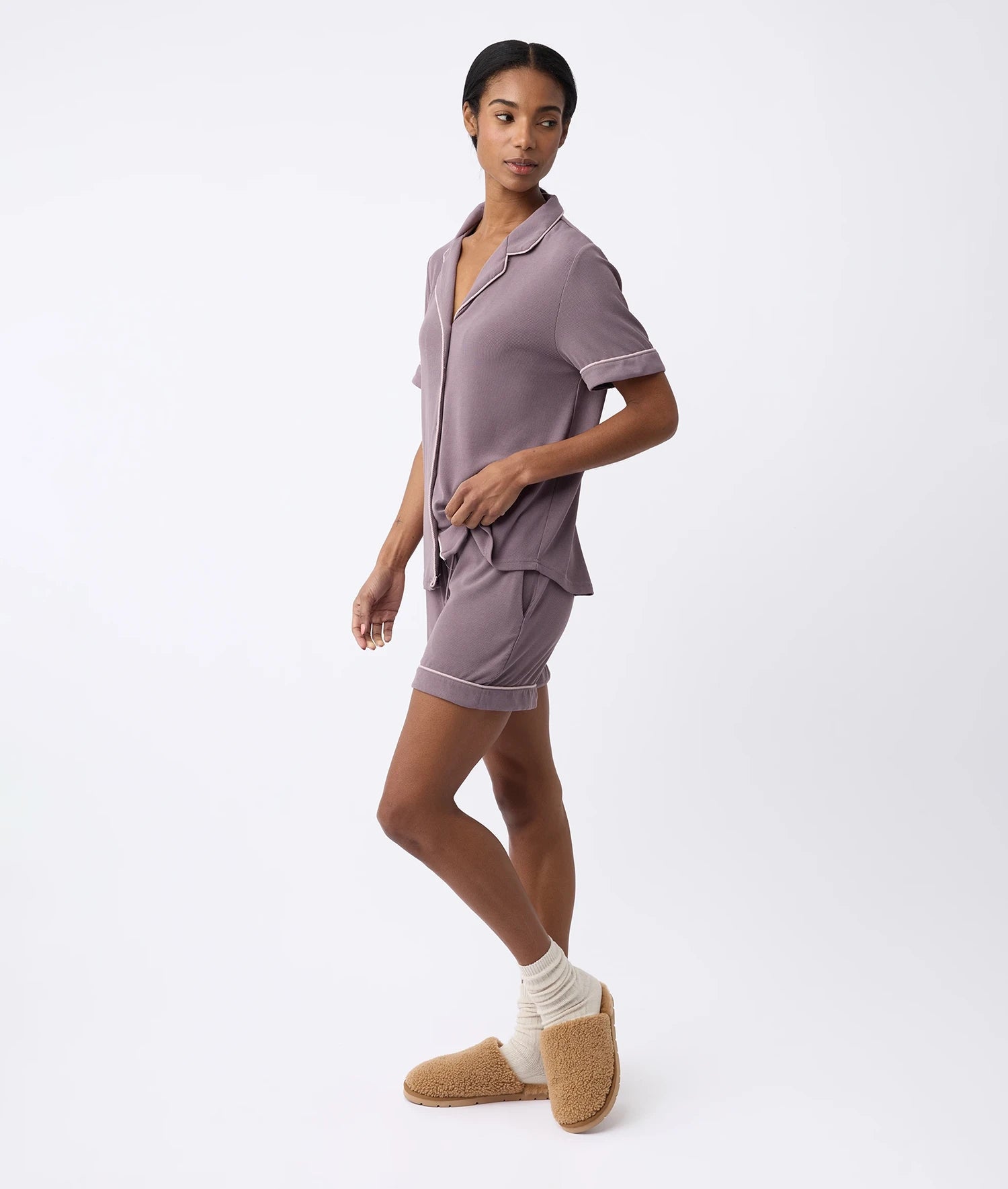 A person in a Cozy Earth purple Women's Bamboo Rib-Knit Classic Short Sleeve Pajama Set with shorts, beige socks, and fluffy brown slippers stands against a plain white background. |Color:Twilight