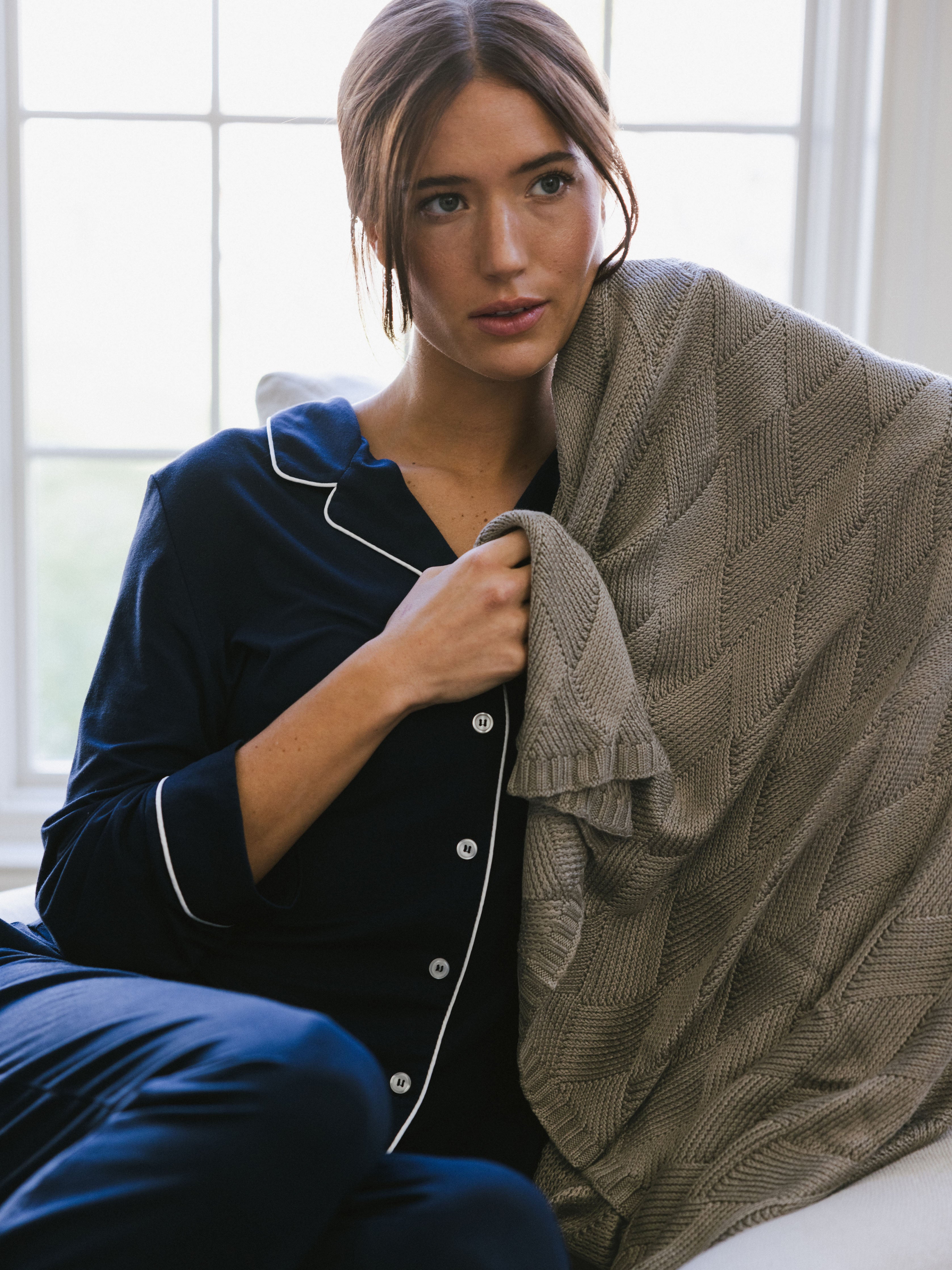 Walnut Diamond Knit Blanket photographed in a home living room. A woman holds the blanket over her shoulder. |Color:Walnut