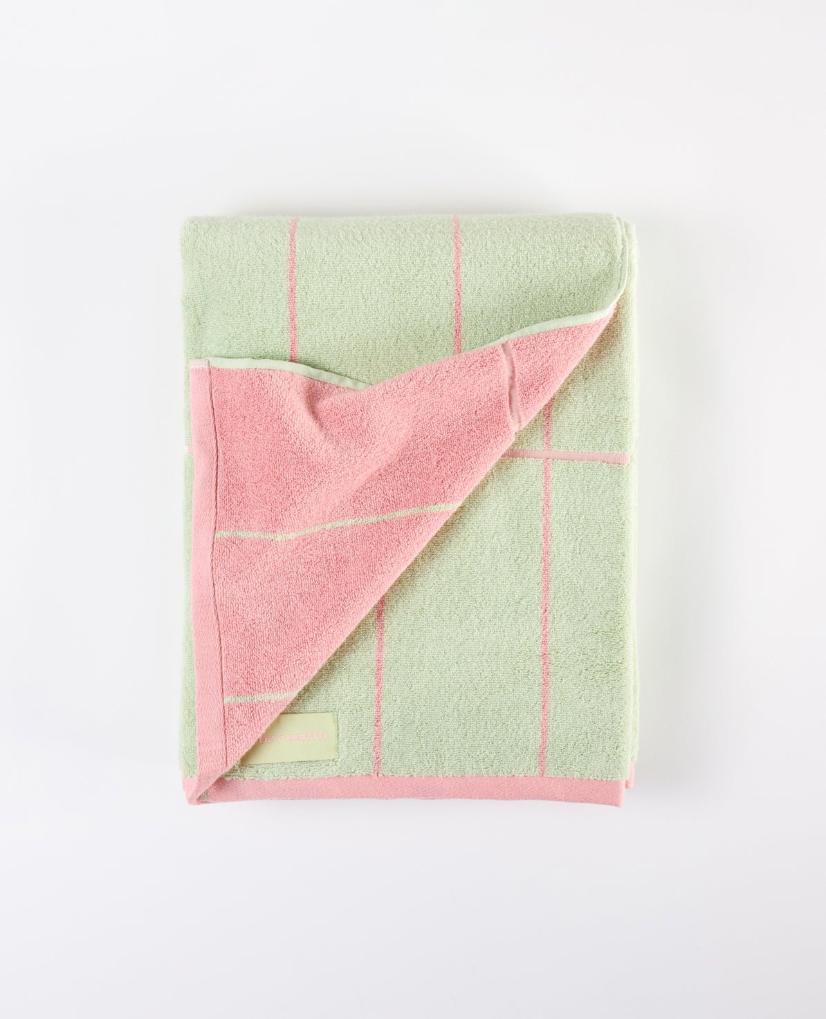 The Windowpane Resort Towel by Cozy Earth is folded on a plain white background. It features a light green design with pink checkered lines and trim, with a corner flipped over to reveal its pink interior. |Color:Watermelon