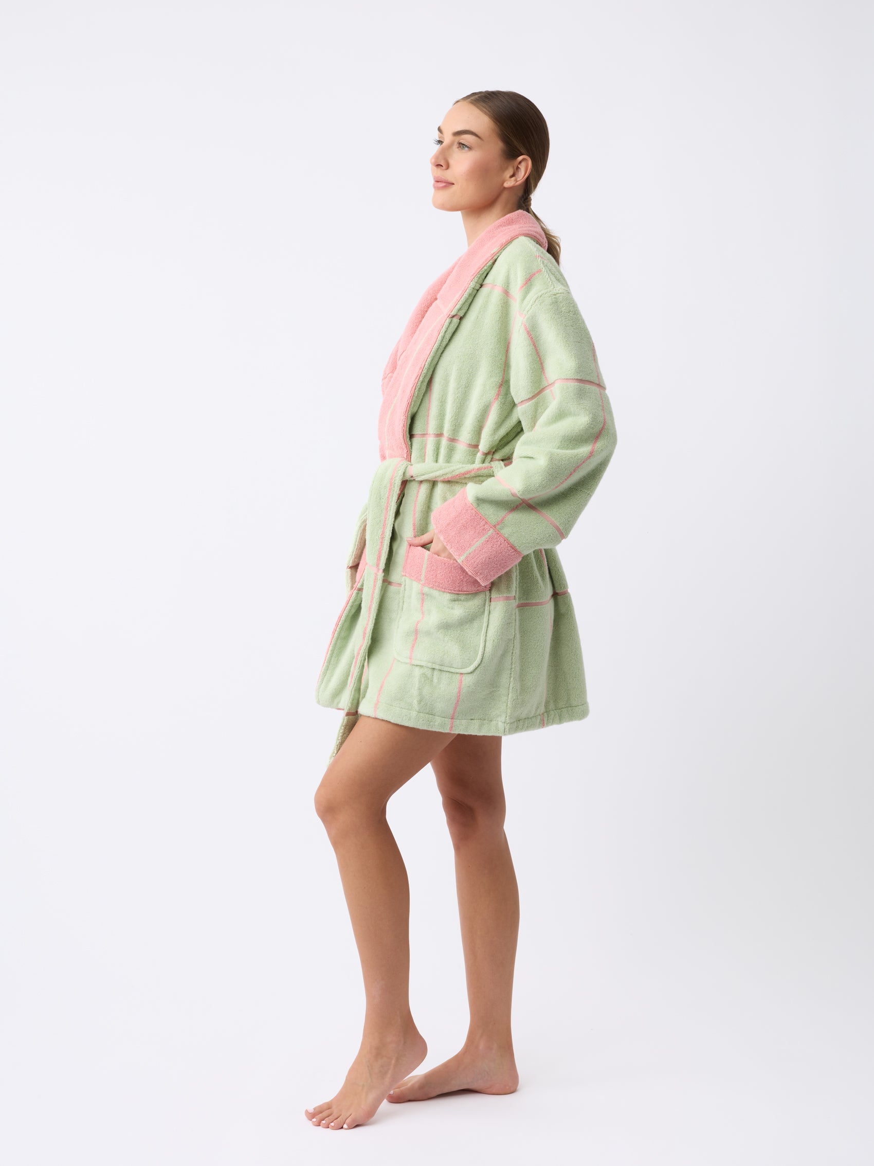 A person stands barefoot on a white background wearing the Cozy Earth Windowpane Resort Robe, featuring pastel green and pink checks with a belt. The robe has pink cuffs and a collar, and the person is slightly turned to the side, looking forward. |Color:Watermelon