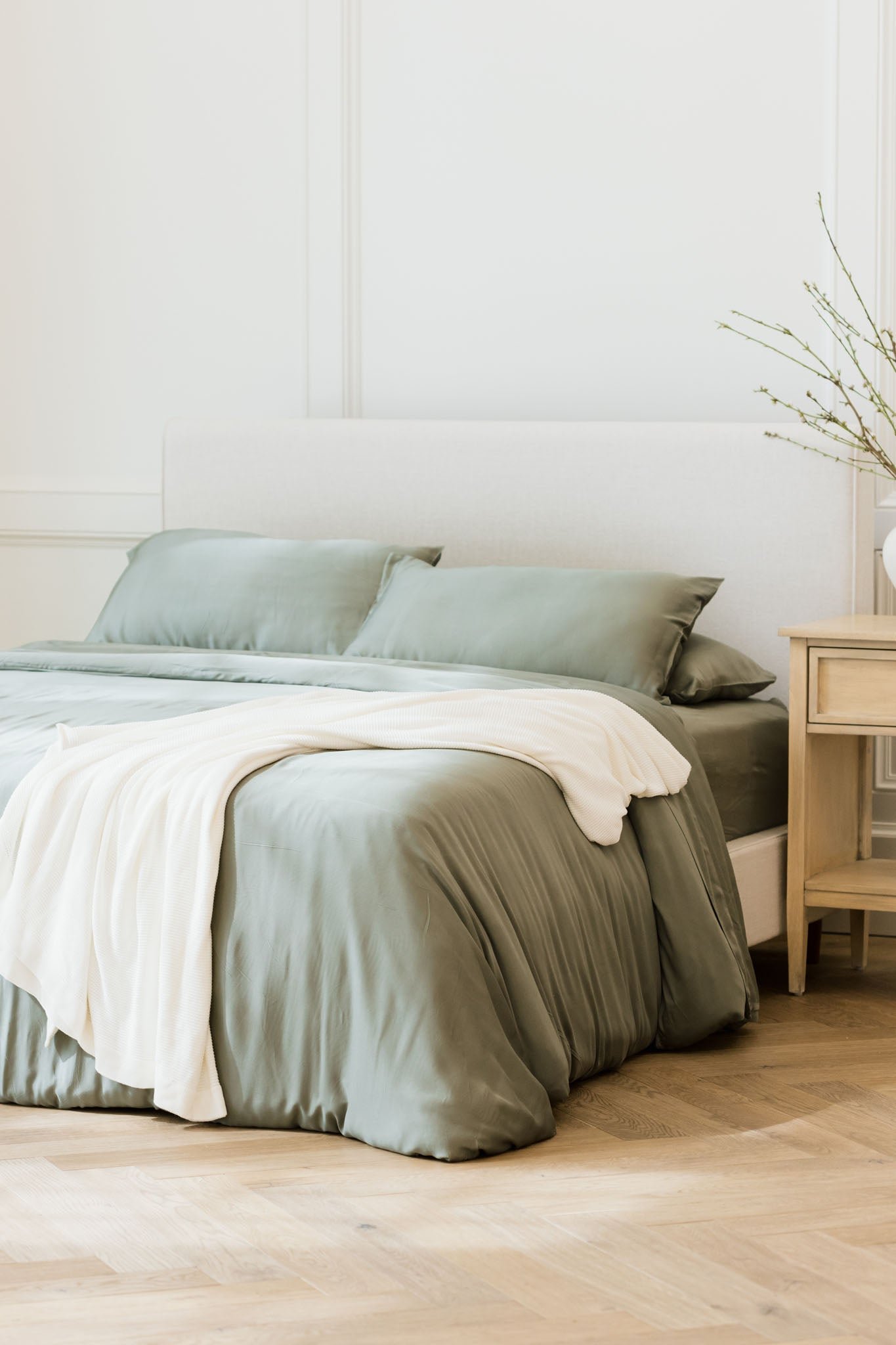 White cloud knit blanket draped over bed with sage bedding 