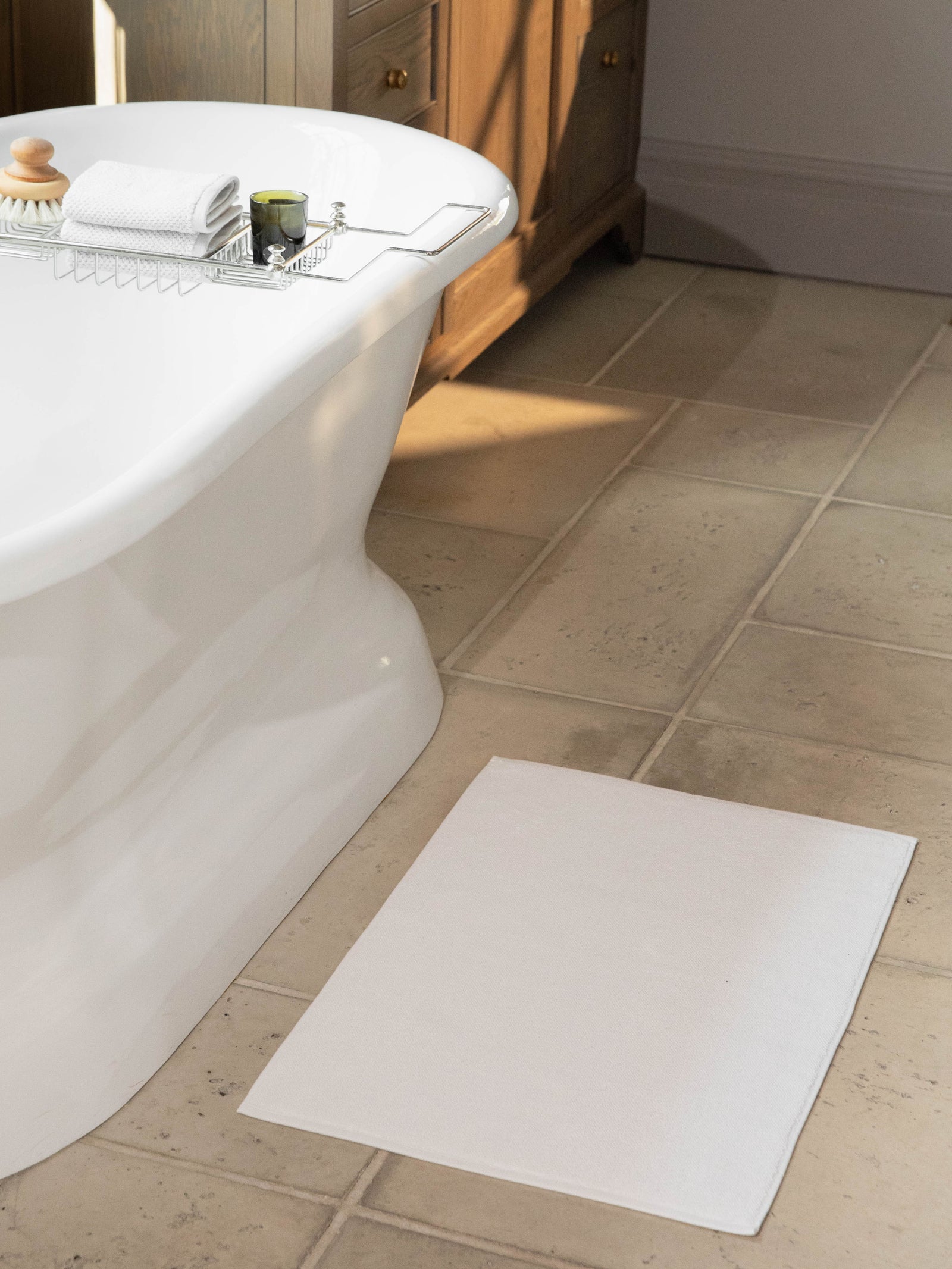 White looped terry bath mat resting on bathroom floor in front of bathtub. 