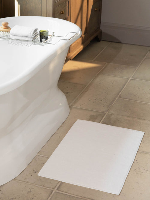 White looped terry bath mat resting on bathroom floor in front of bathtub. |Color:White