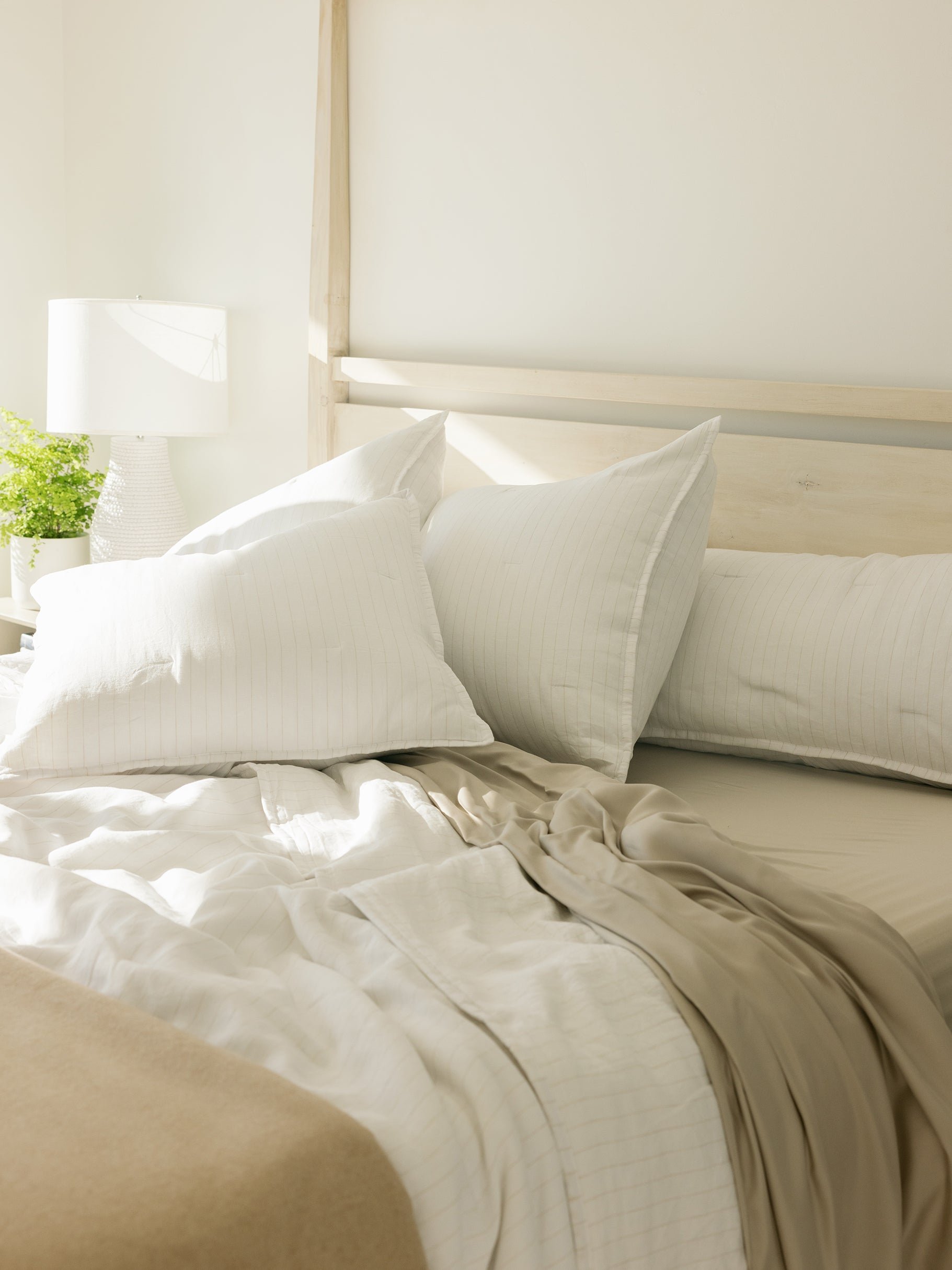 Unmade bed with flax pencil stripe shams on the pillows 