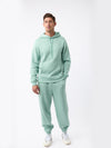 A person is wearing the Men's CityScape Hoodie from Cozy Earth in mint green, paired with matching sweatpants, standing against a plain white background. They complete their outfit with white sneakers featuring green details. |Color:Wintergreen