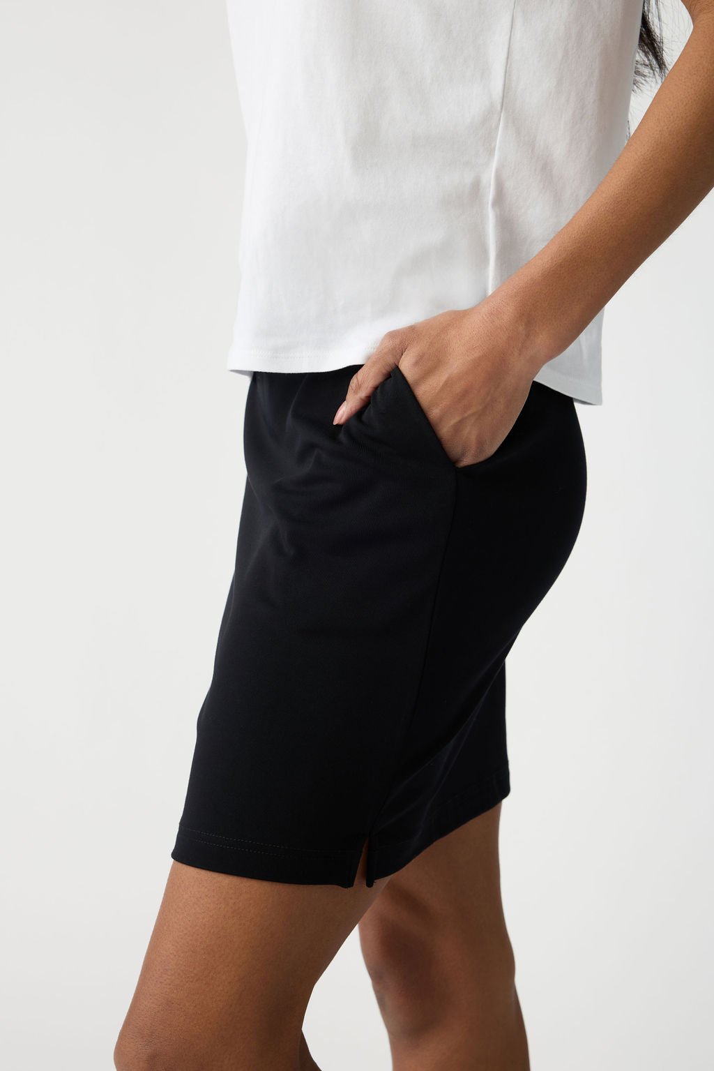 A person in a white top and Cozy Earth's Women's Brushed Bamboo Skirt, featuring a small side slit, stands with one hand in their pocket against a plain, light background. |Color:Black