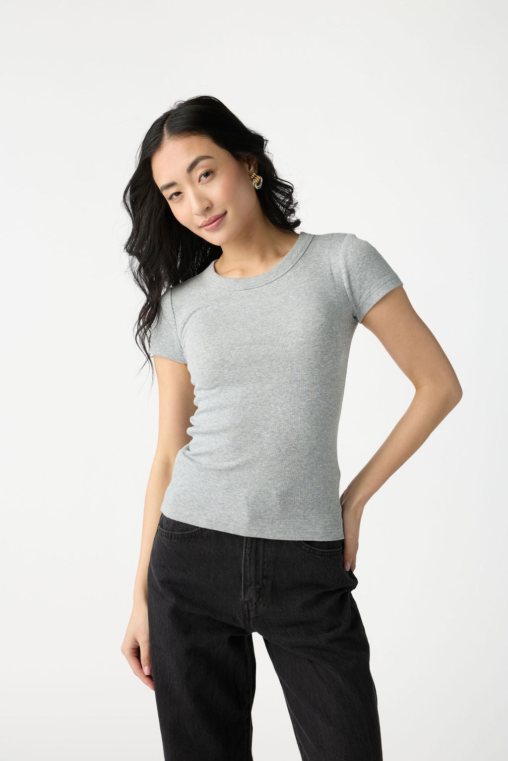 A dark haired woman wears Cozy Earth Women's Fine Ribbed Tee in Heather Grey. She is wearing black jeans and stands in front of a white background. |Color:Heather Grey