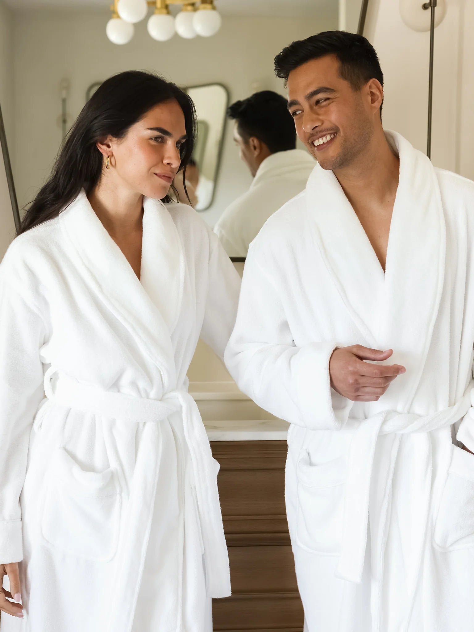 A man and woman wearing white Cozy Earth Luxe Bath Robes stand in a bathroom.