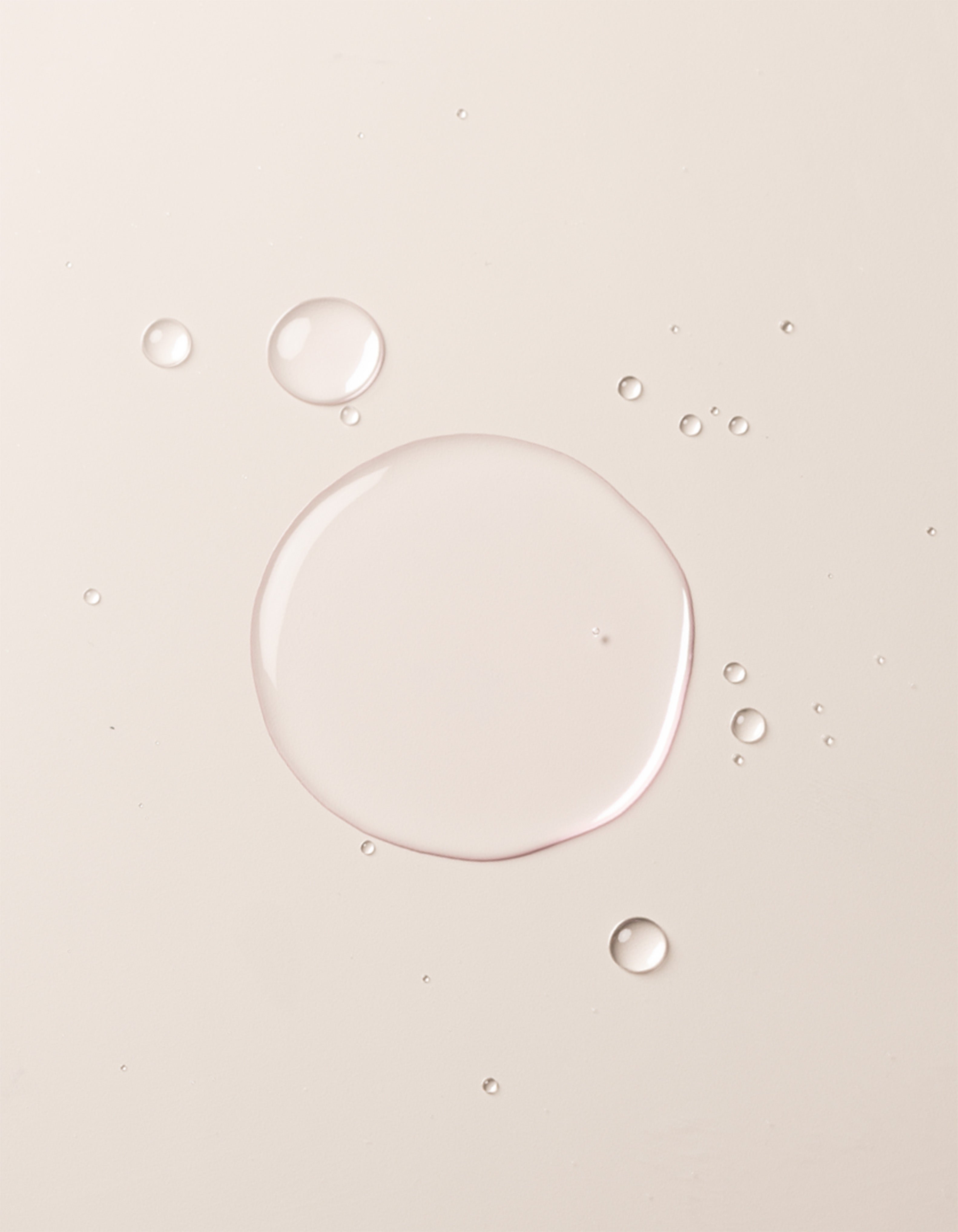 A close-up image showcases translucent liquid droplets of Cozy Earth's Balancing Face Mist on a smooth, off-white surface. The droplets vary in size, with one large central droplet surrounded by several smaller ones, creating a clean and minimalistic appearance. |Size:Full Size