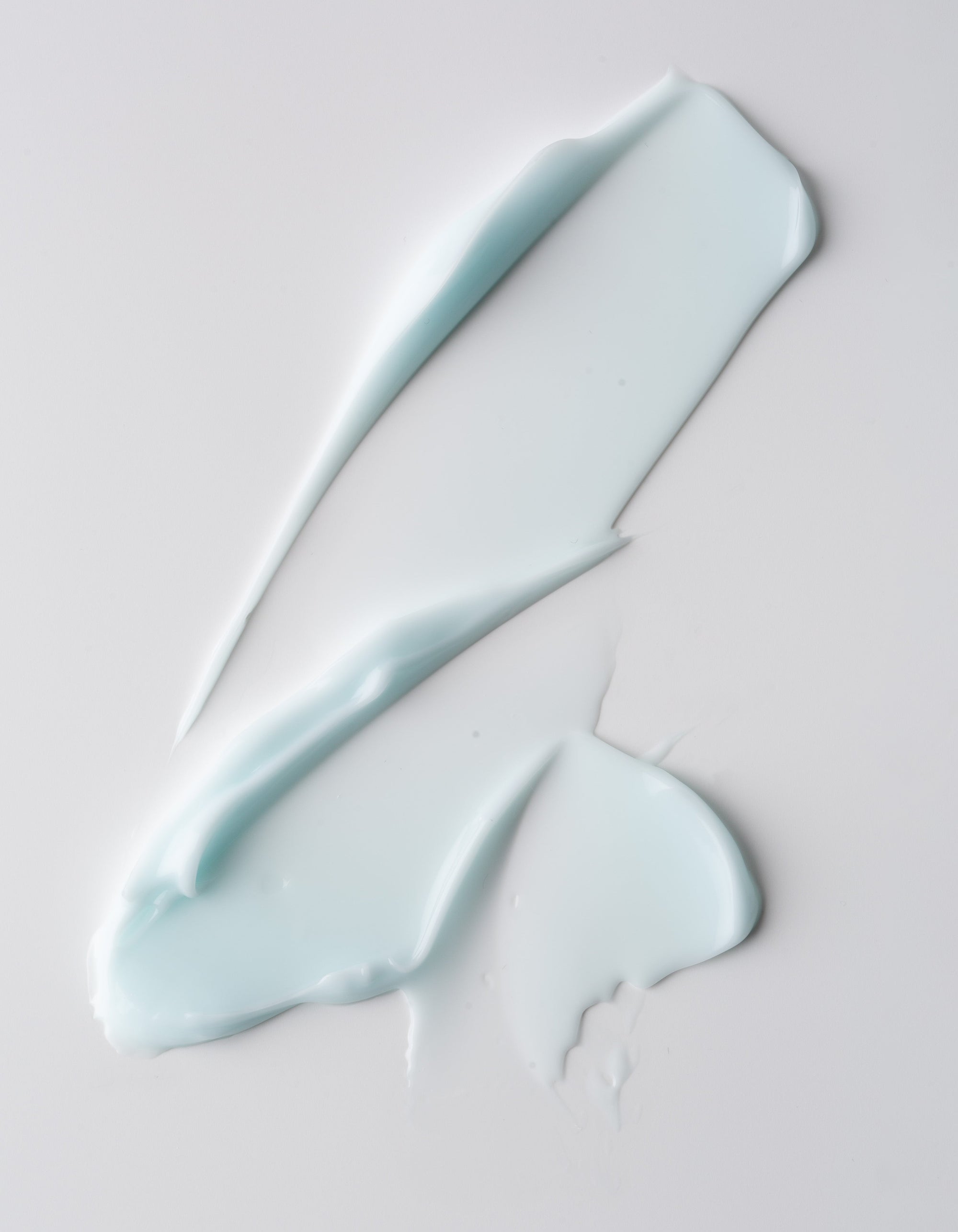 A smear of the Water Cream Moisturizer by Cozy Earth spread on a white surface, showcasing its smooth texture and slightly glossy light blue finish. 