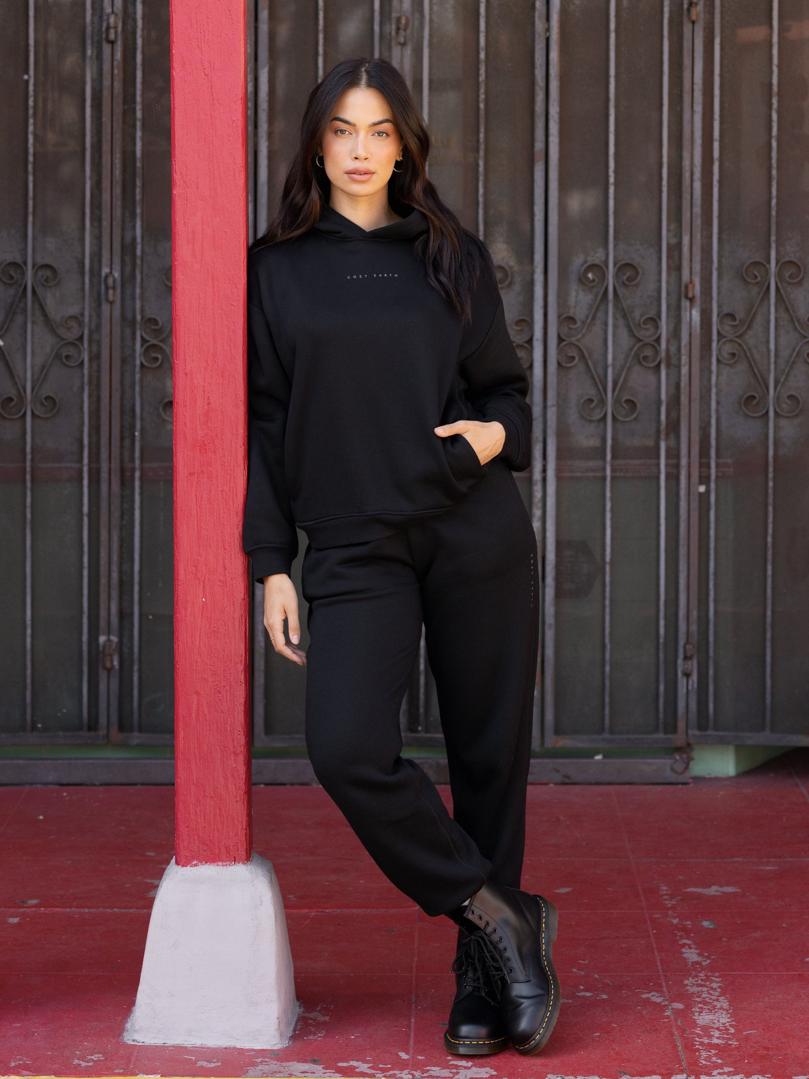 Black CityScape Joggers. The Joggers are being worn by a female model. The photo is taken with the models hands by the pocket of the joggers. The back ground is a downtown area. 
