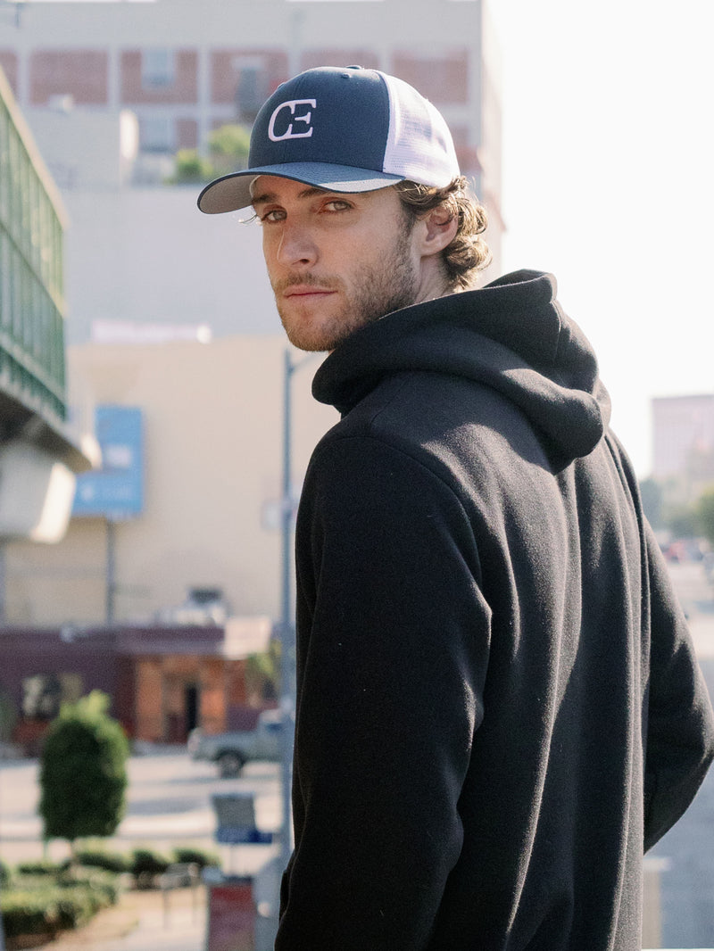 Man wearing a black cap with a CE logo with a city street in background
